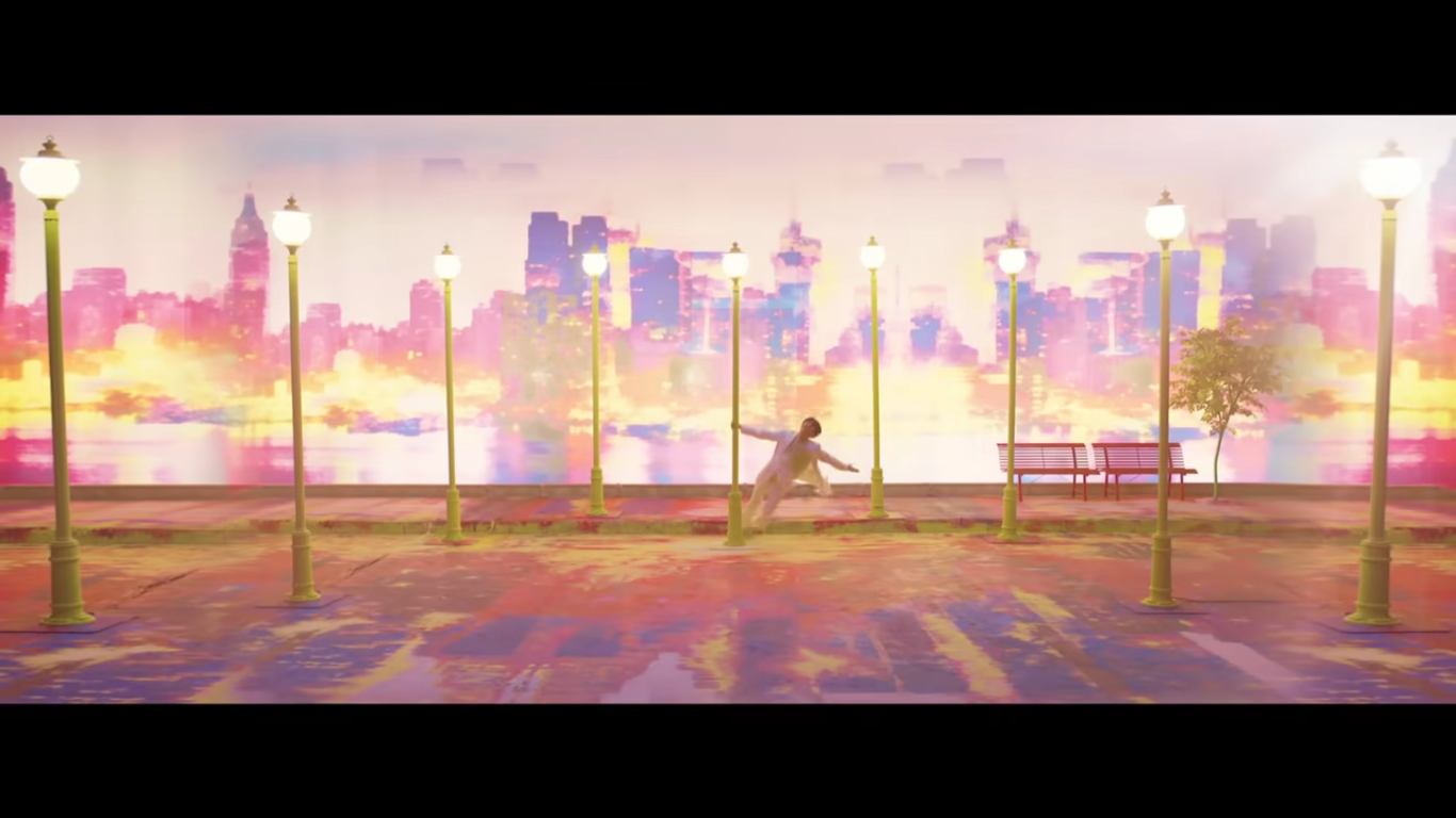 A member of BTS hangs off a light post surrounded by other light posts in front of a water color city scape. He is wearing all pink, the light posts are all yellow. and the city scape is yellow, purple , and pink.
