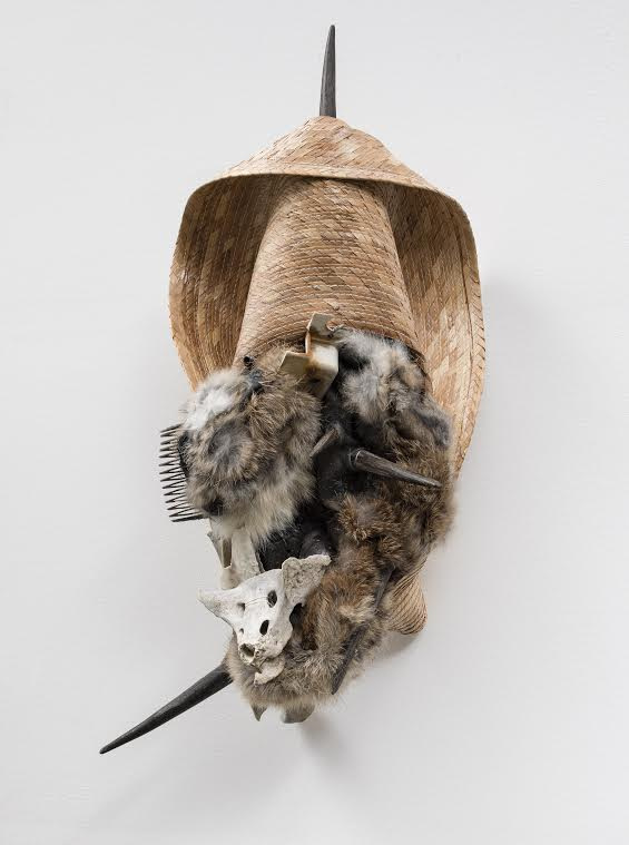 A sculpture features many shades of fur, a wicker-like material, and wood tusks. The materials altogether form an oval-like shape.