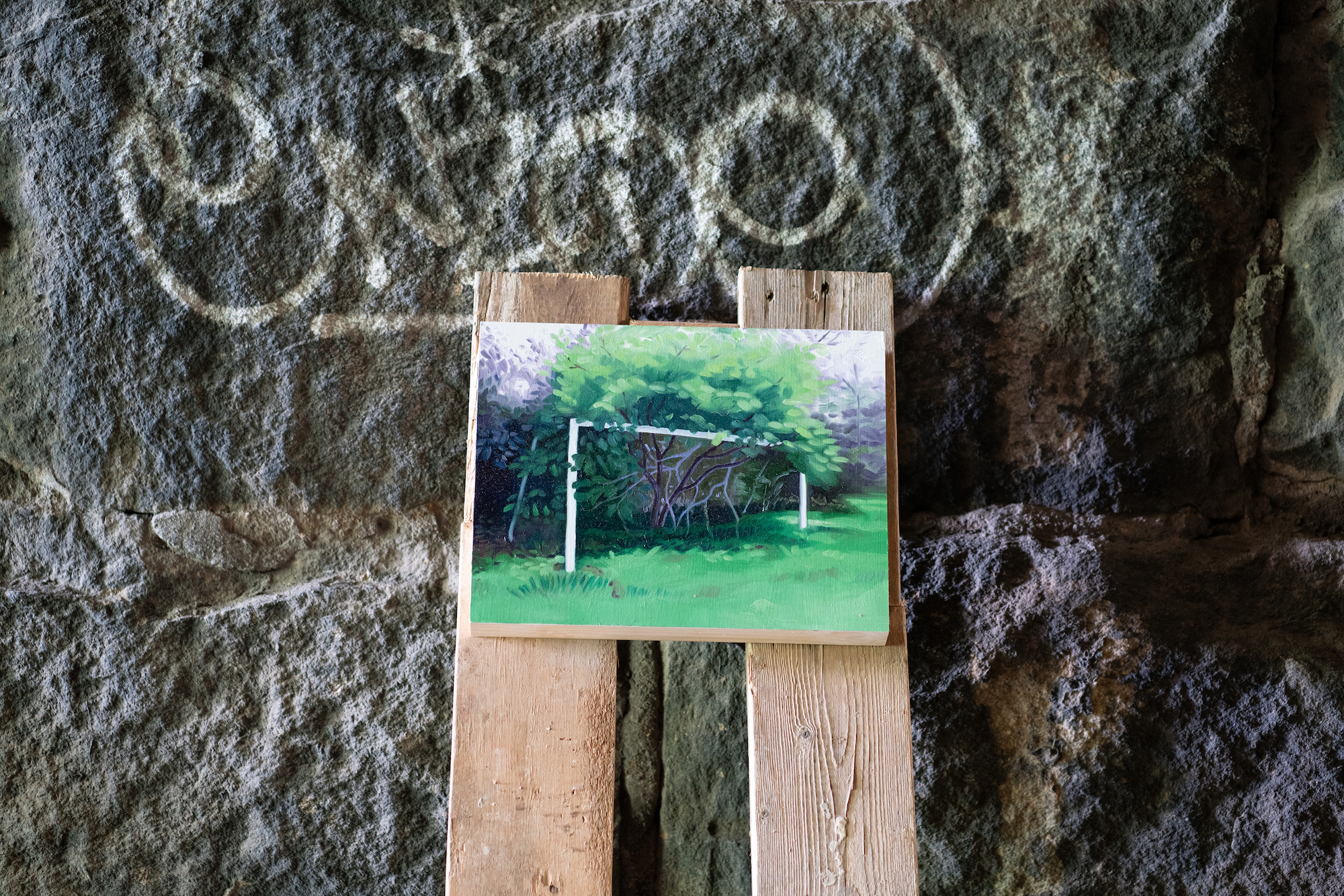 A small painting of a green tree leans against a stone wall. The wall is gratified with white paint.