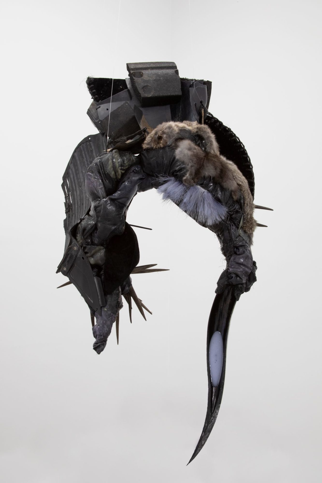 A grey and black animal-like sculpture hangs suspended by strings.
