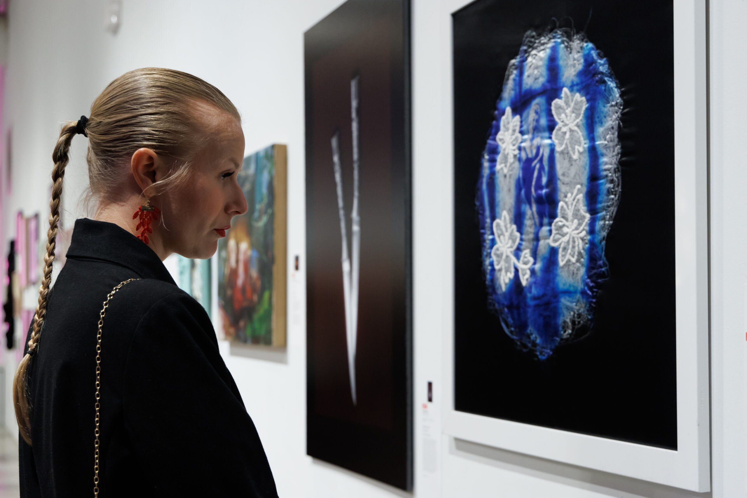 Image of a blond woman observing a black art piece with blue and white details.