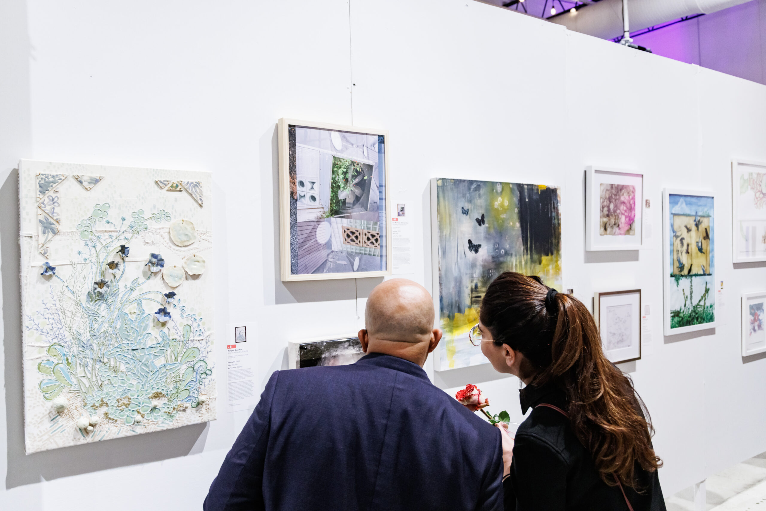 Image of a man and woman looking at a white wall featuring many different art pieces.