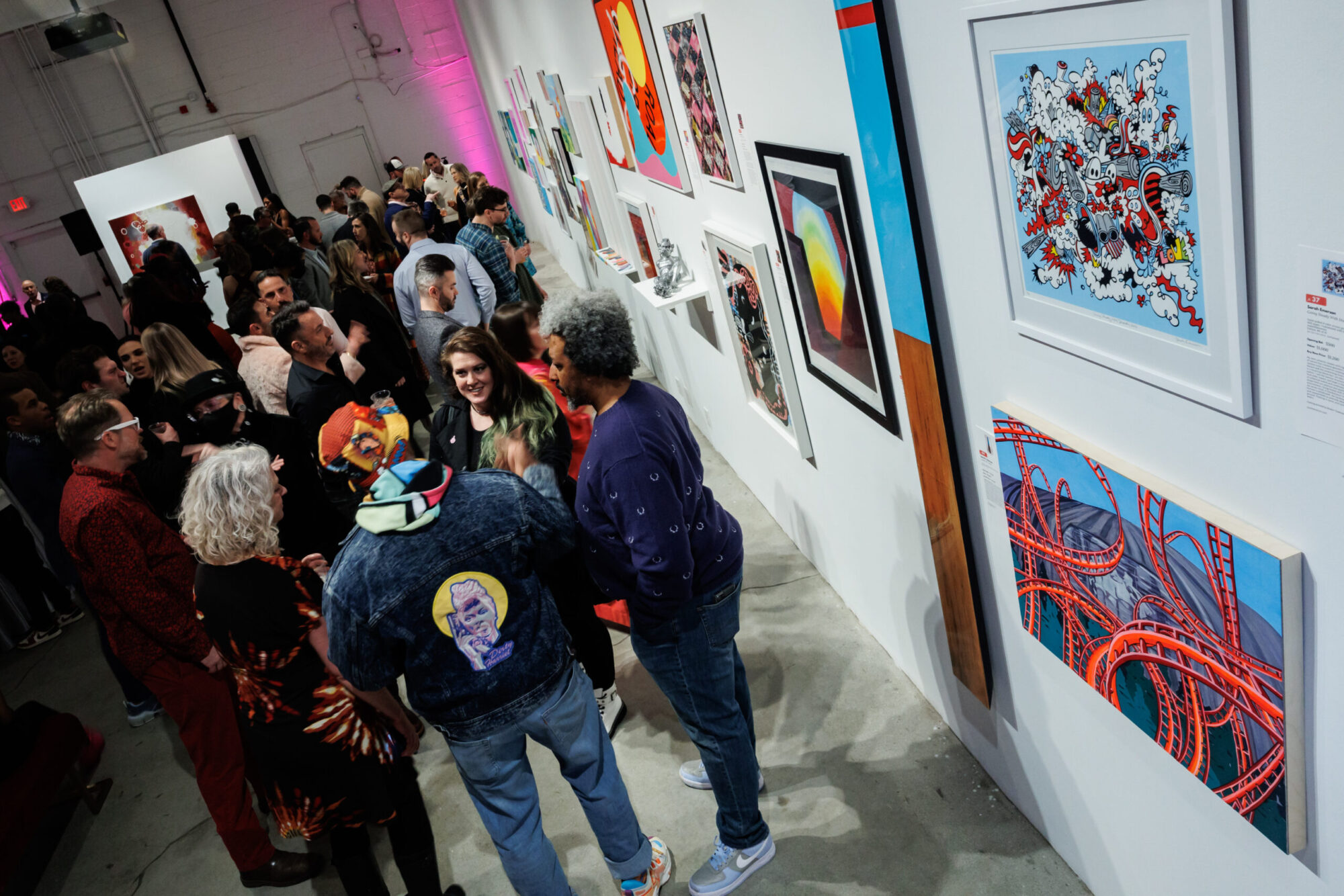 Image of a crowd of people gathering next to a wall of a variety of framed art pieces.