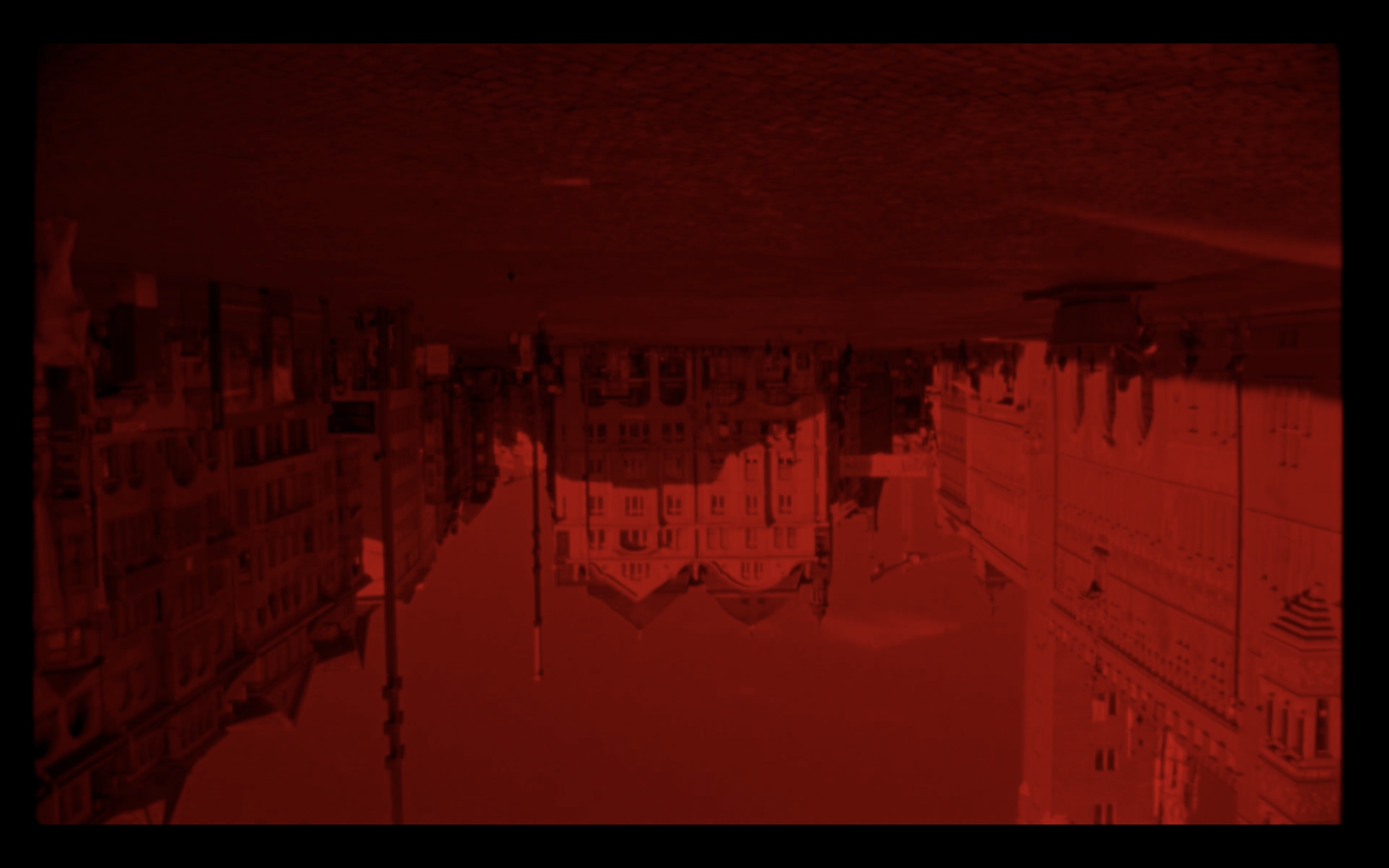 An upside-down image of a plaza surrounded by buildings. The entire image is cast in a blood red hue.