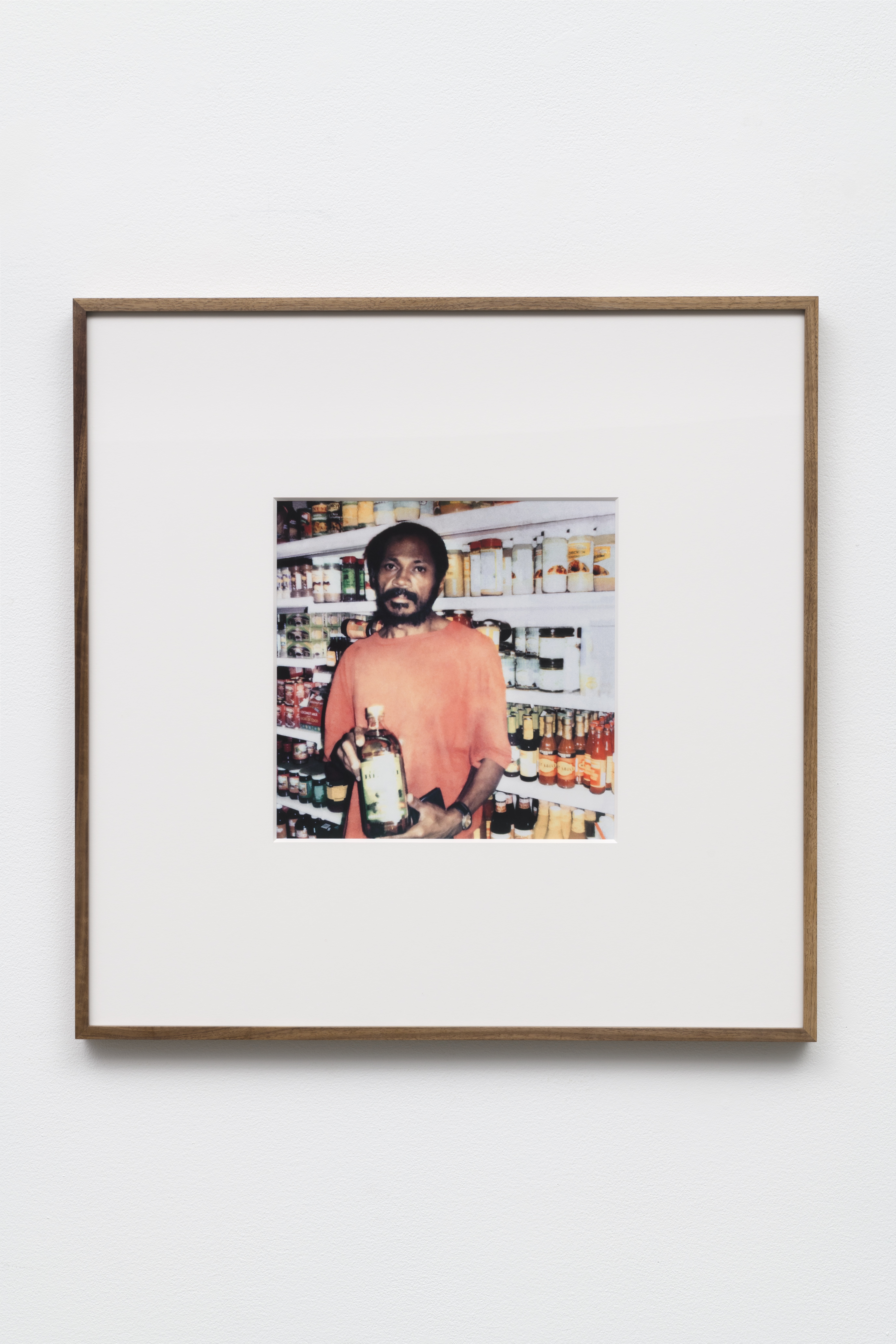 This is a photograph of a framed photograph of a man in a grocery holding a bottle taken by artist Mohamed Bourouissa