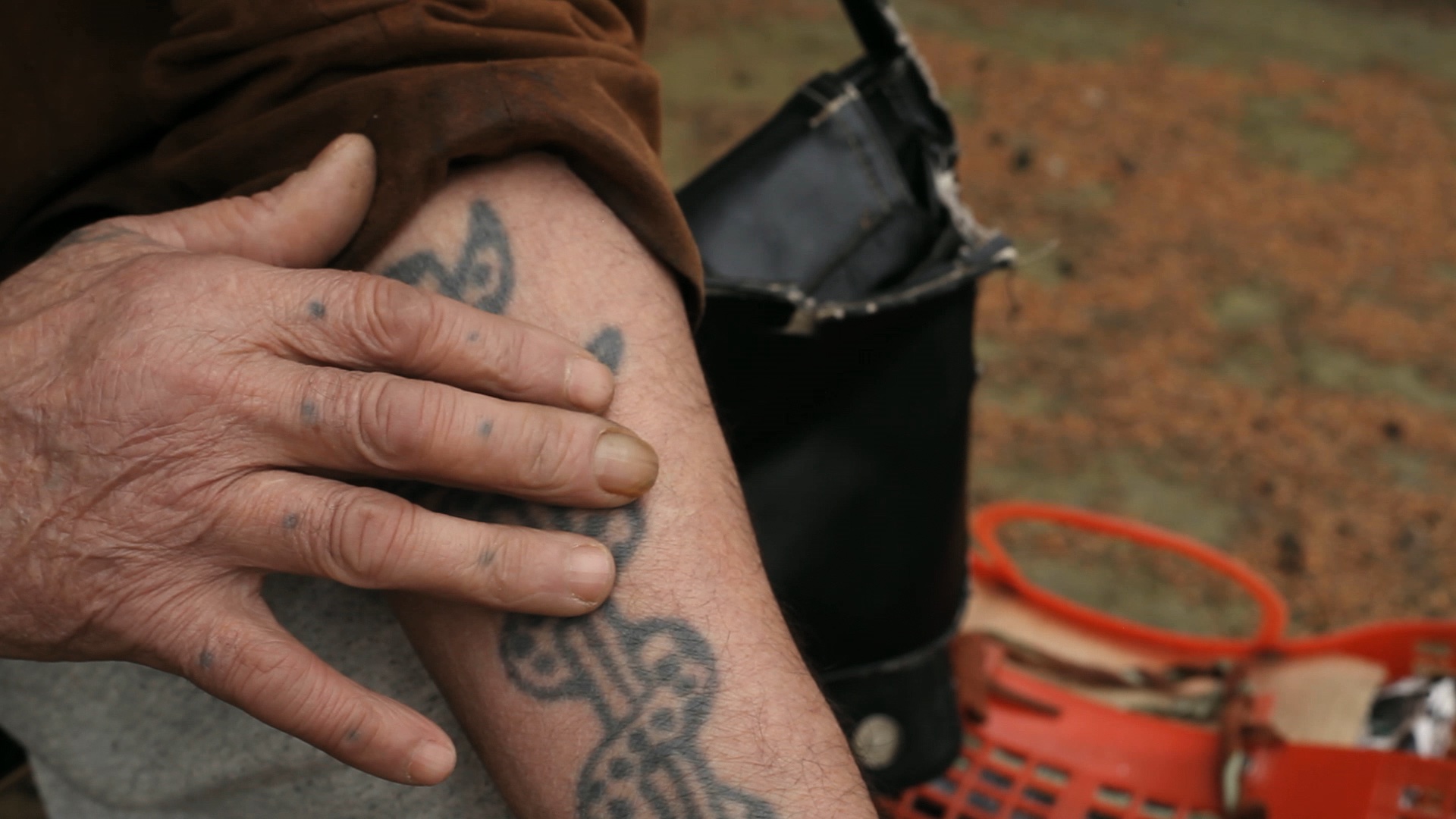 This is a photograph of a person running their hand along their tattoo on their right forearm taken by artist Mohamed Bourouissa