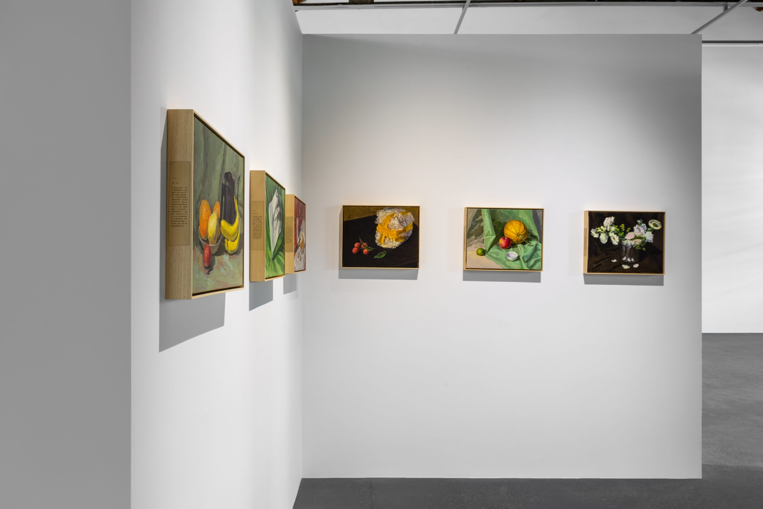 A row of paintings of various still lifes by the artist Ge Yulu, hung upon a stark white wall