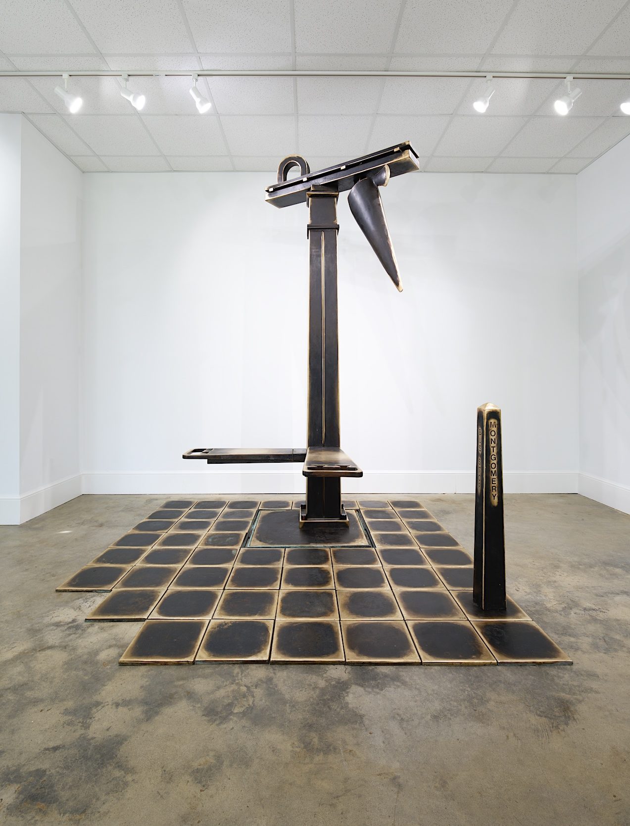 A stark white room is filled with a large bronze sculpture recreating a bus stop.