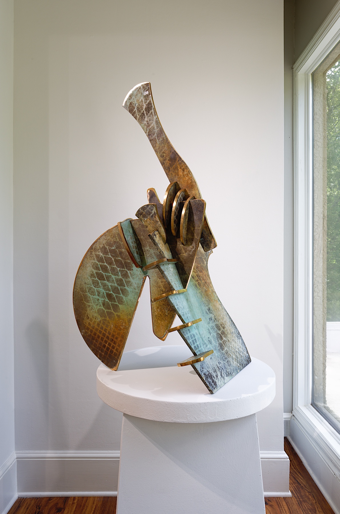 A green and gold patina'd bronze sculpture rests atop a white pedestal in the gallery.