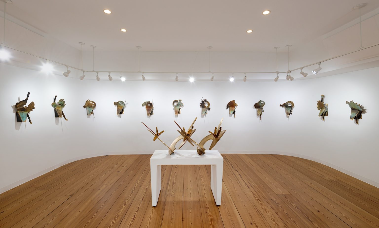 Gallery walls are adorned with 12 wall sculptures with a single gold sculpture in the middle upon a white pedestal amid the oak gallery floors.