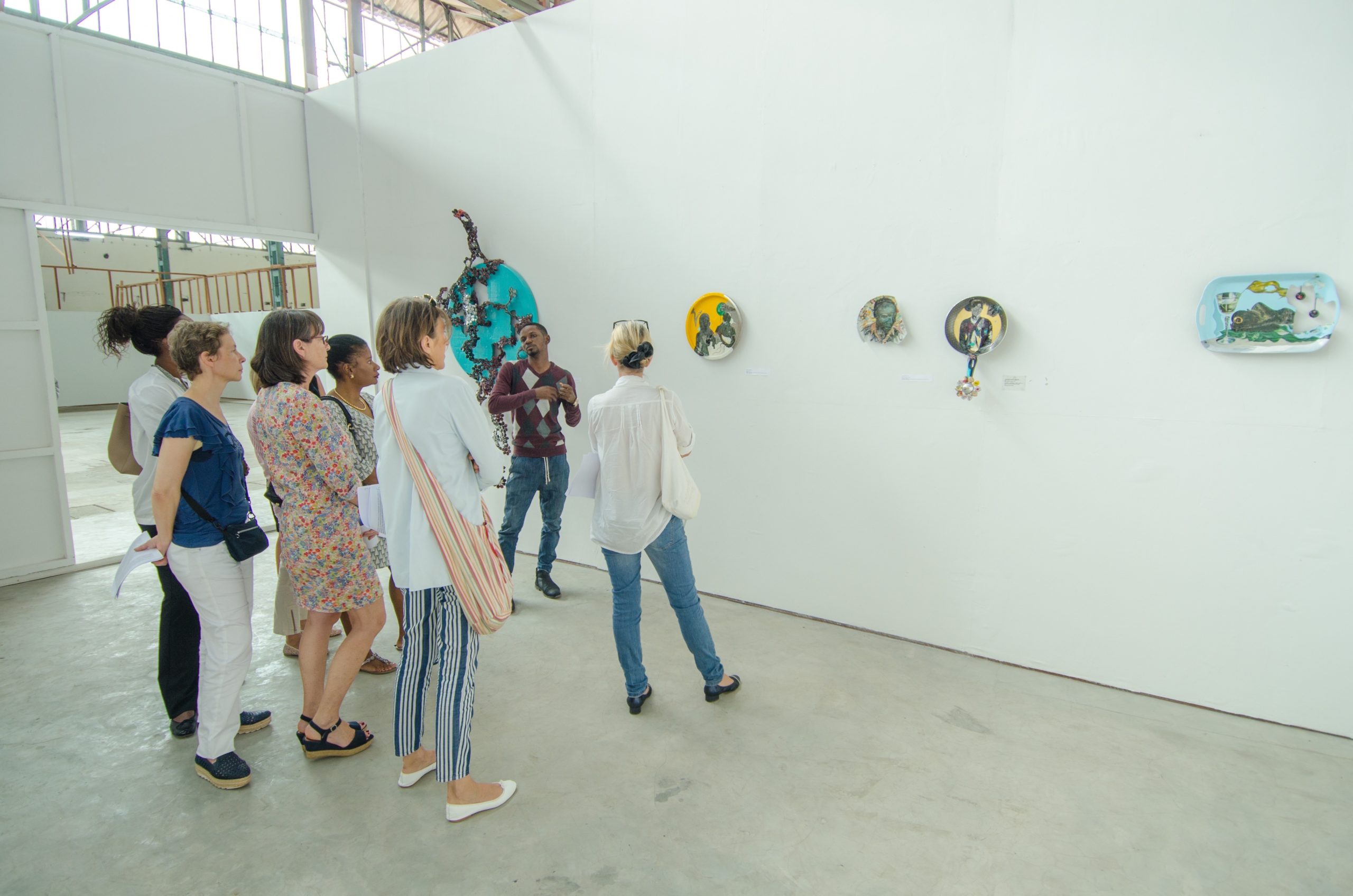 Image of a group of people viewing art pieces hanging on the wall with a guide. Photo provided by courtesy of the artist.