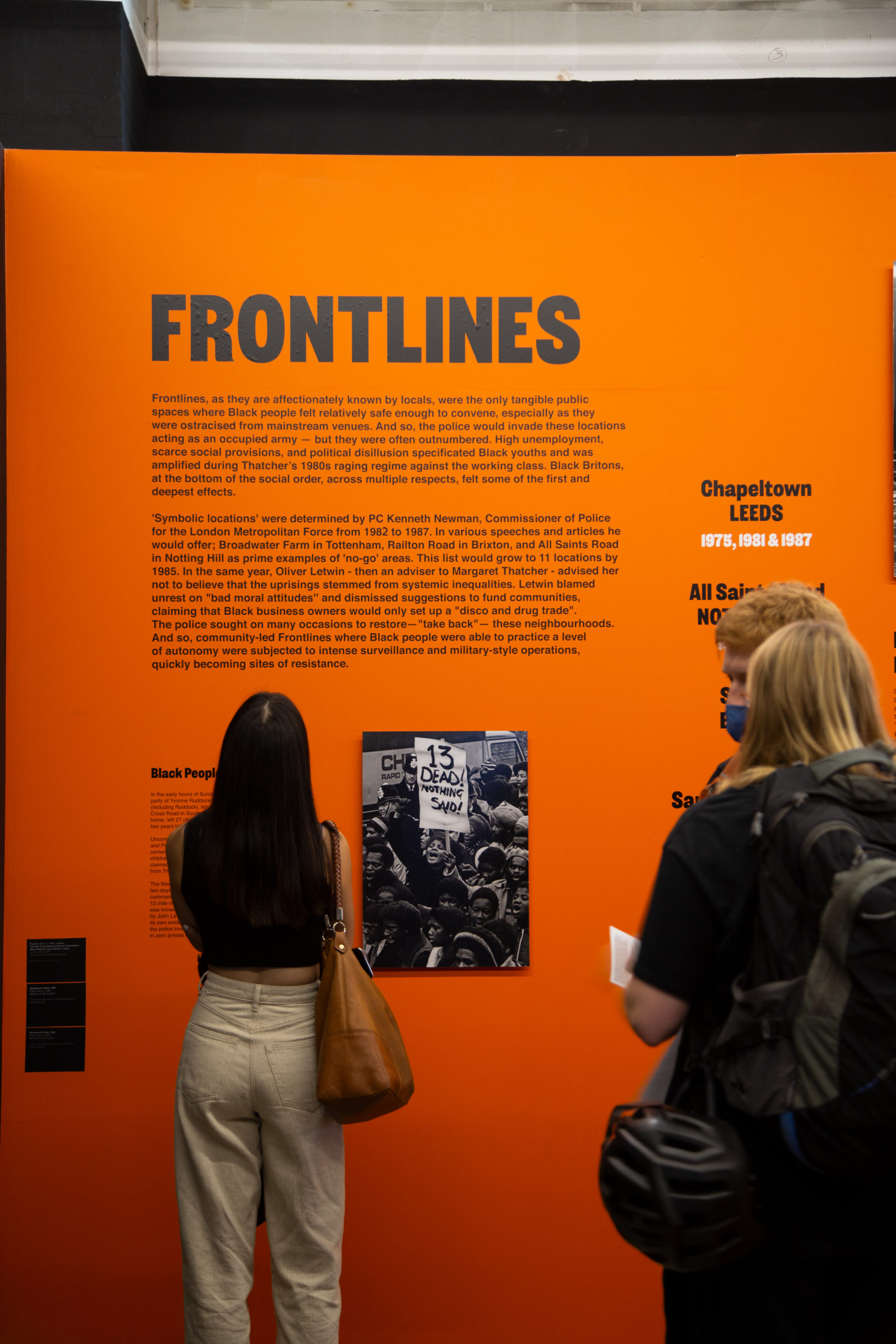 Several people standing in front of an orange wall with a photo of protestors and text that describes the significance of 