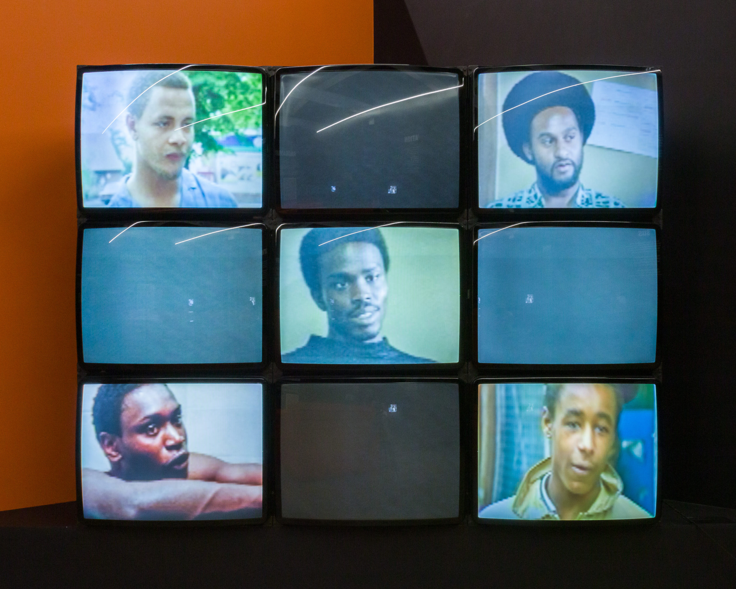 A 3x3 set of screens placed edge to edge. Photo portraits are displayed on the five screens: the one in the middle and the four in the corners.