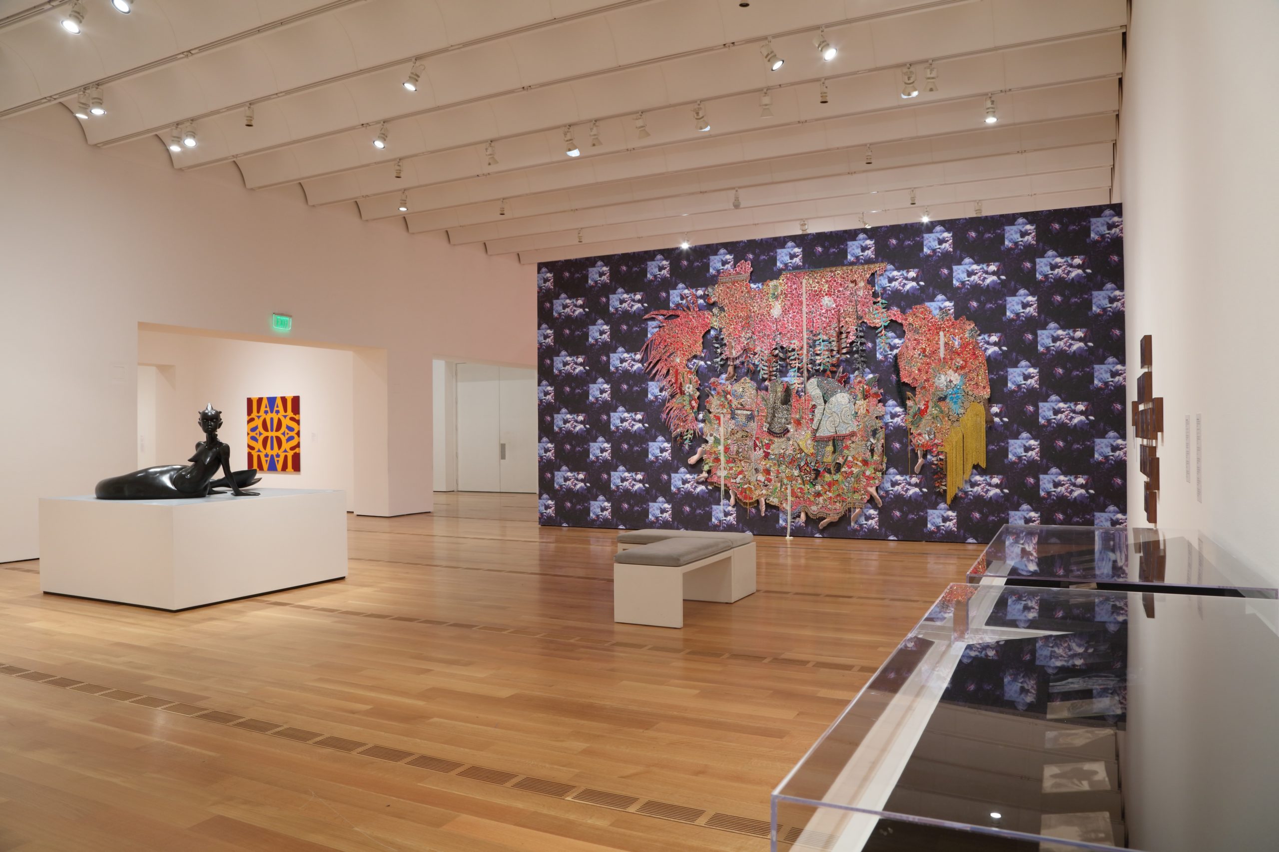 A large, open room with several works of art in it. On the left a mermaid sculpture in visible, with a graphic far behind it. In the center of the view is a wall with graphic art on it.