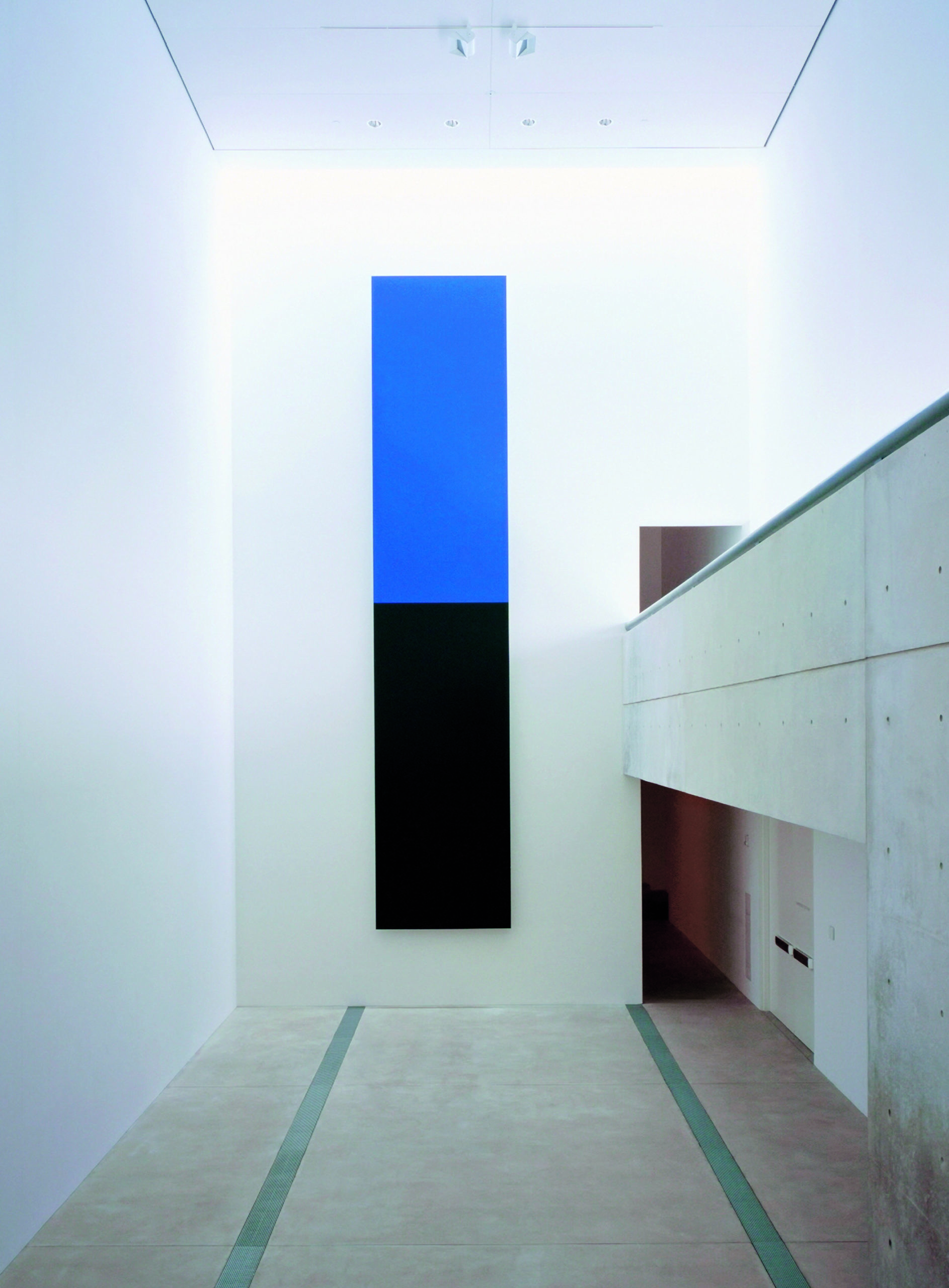 A long vertical piece of art mounted on the wall, with the bottom half black and the top half blue.