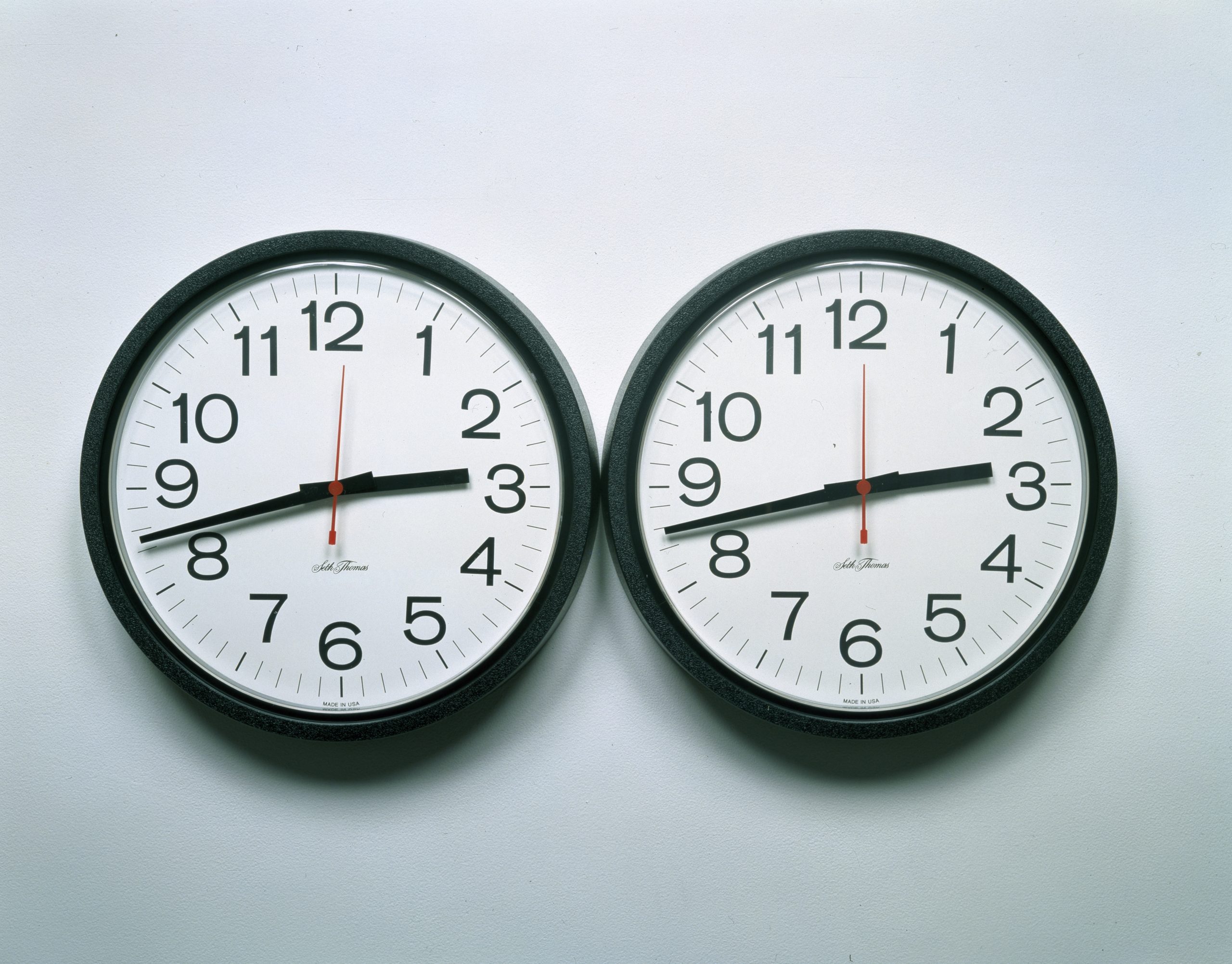 Two clocks with the same time right next to each other on the wall.