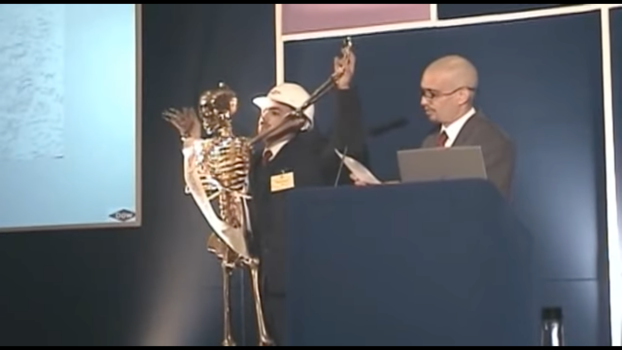 The Yes Men present at a London conference while holding up Gilda the golden skeleton.