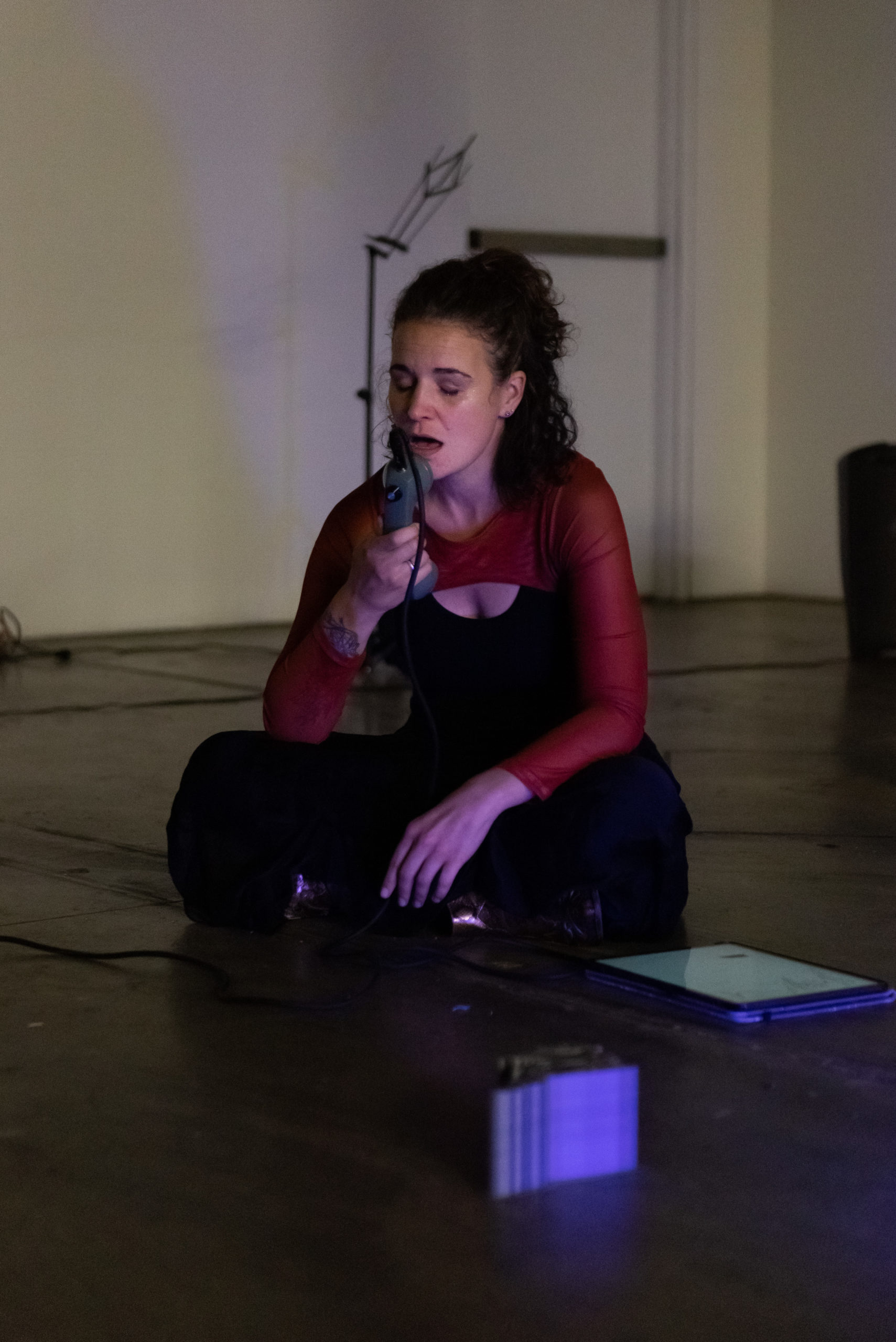 A woman sits on the ground speaking into a telephone receiver in a dimly lit room