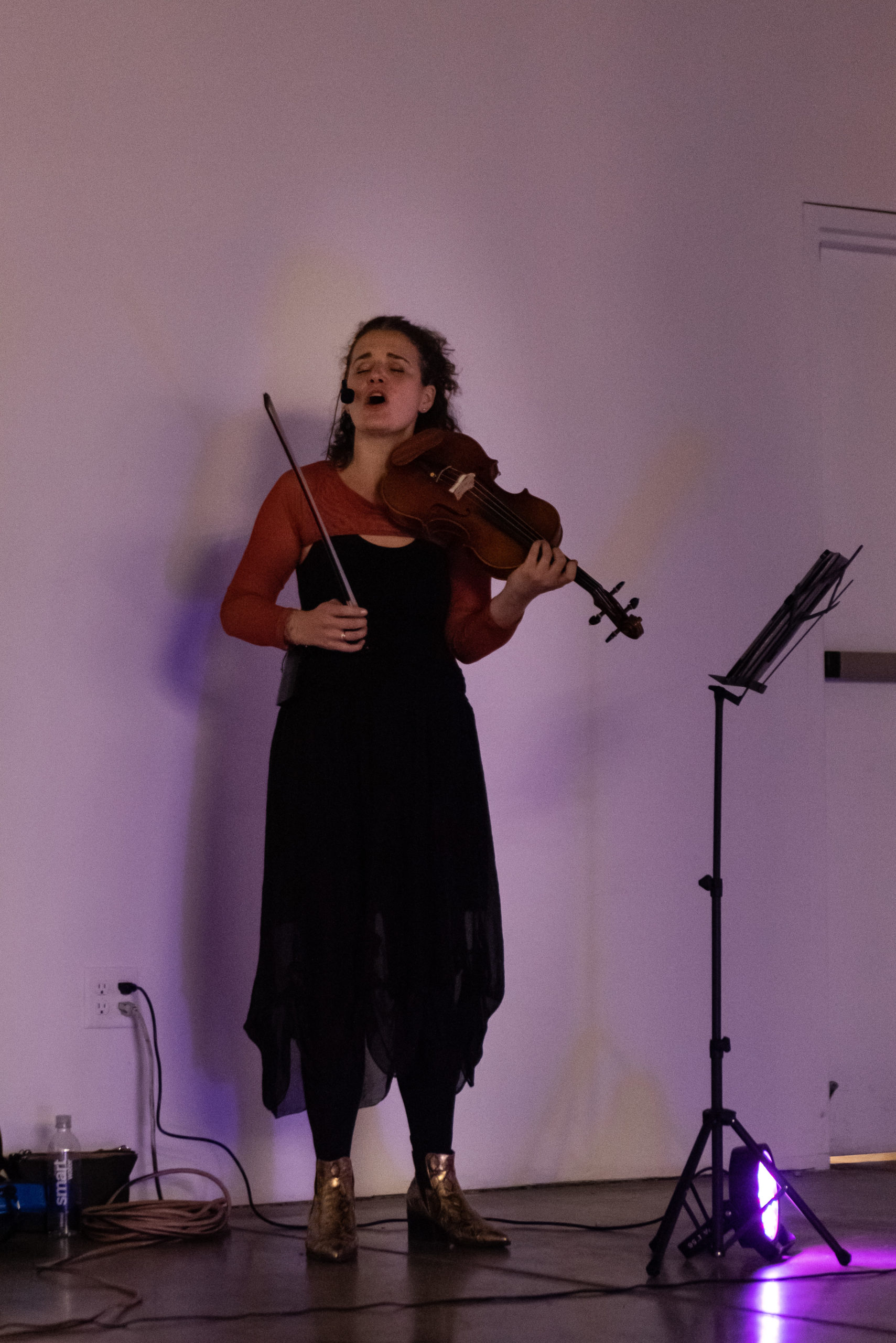 A woman standing, holding a violin, mouth agape, sings