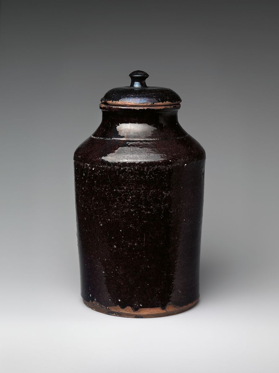 A dark and glossy covered jar set within a gray background.