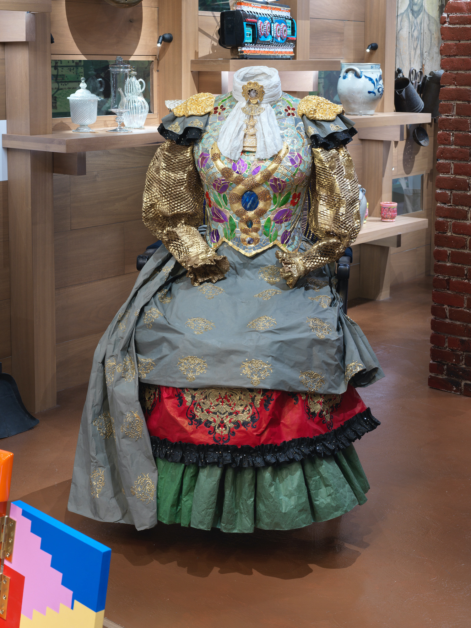 A dress inlaid with gold and crystals, mosaic tiles set against a light brown wooden interior.