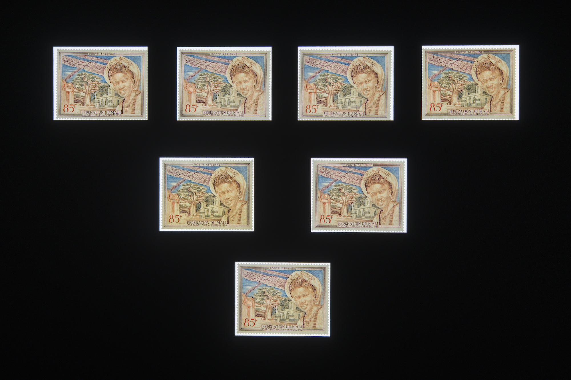A series of seven identical stamps depicting a woman and a landscape with a building behind her, float against a black background, arranged in a symmetrical pattern.