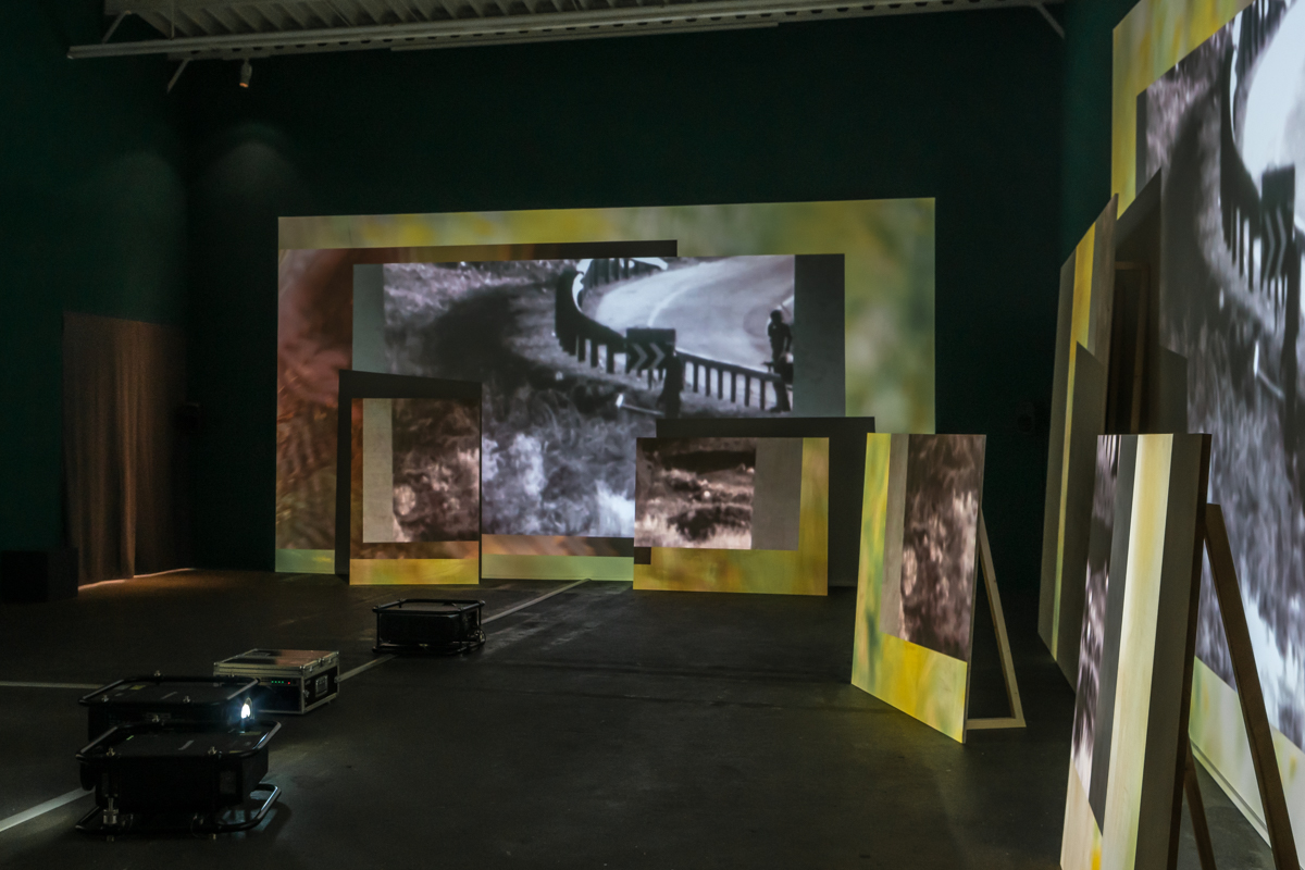 Four different projectors display different black and white footage with yellow-green backgrounds onto different sizes of large wooden boards.