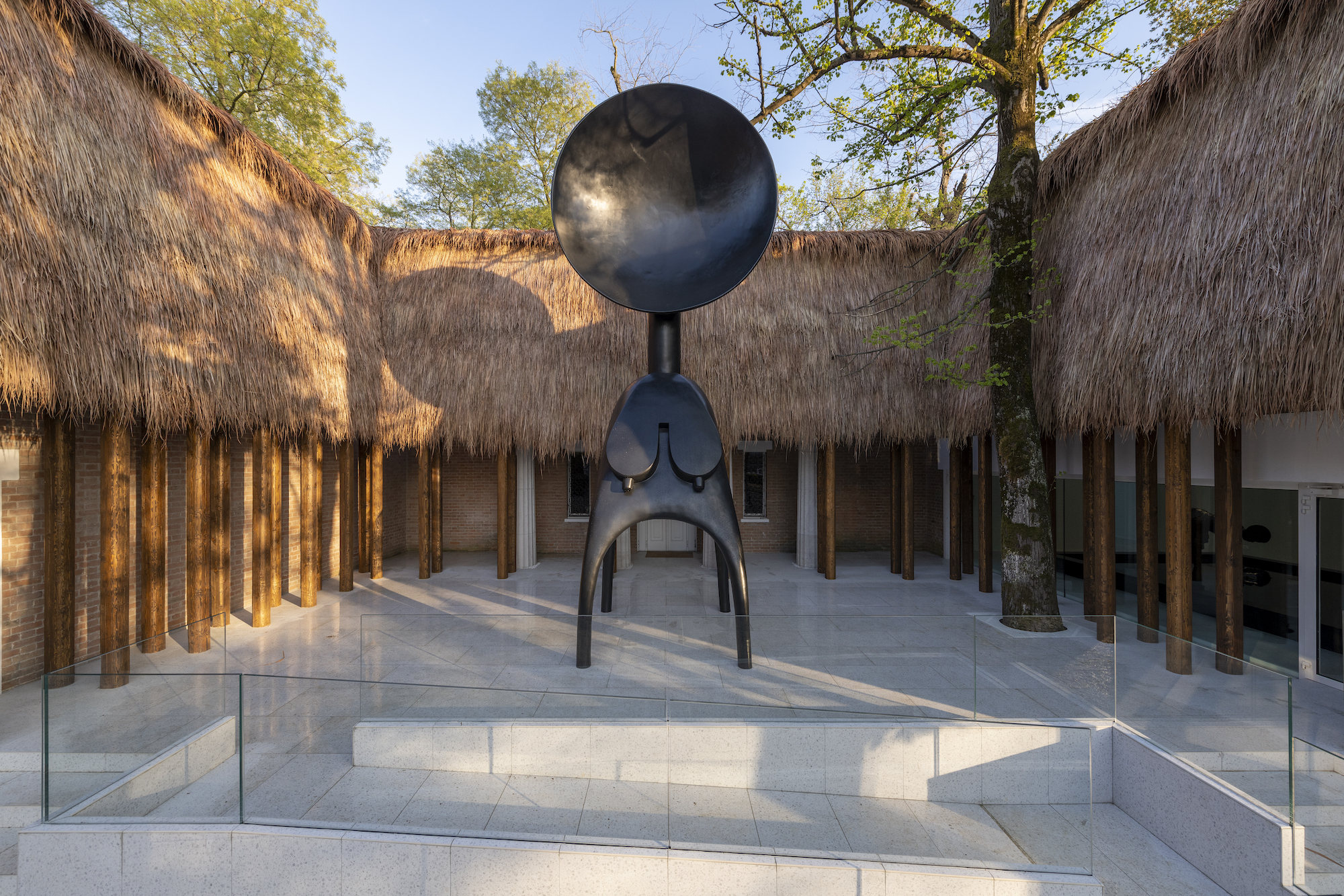 A large black bronze sculpture of an abstracted anthropomorphic figure stands amidst a courtyard.