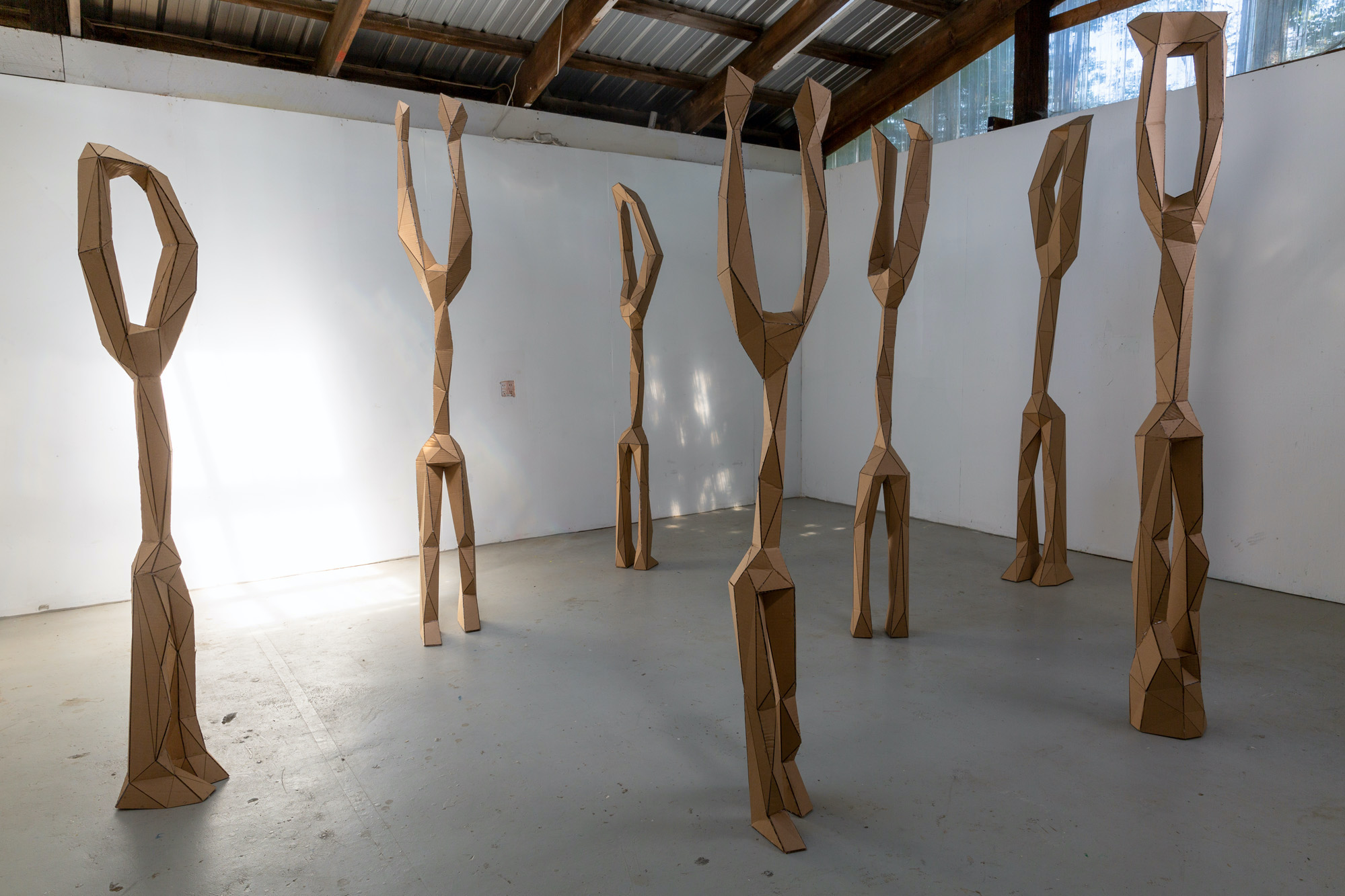 seven abstracted figured standing in a gallery space resembling figures with their hands up.