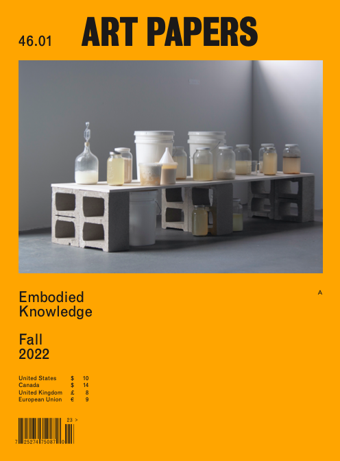 An orange cover with the words ART PAPERS EMBODIED KNOWLEDGE FALL 2022 on it in black lettering and a shelf of jars filled with transparent tan liquids atop cinderblocks in the middle
