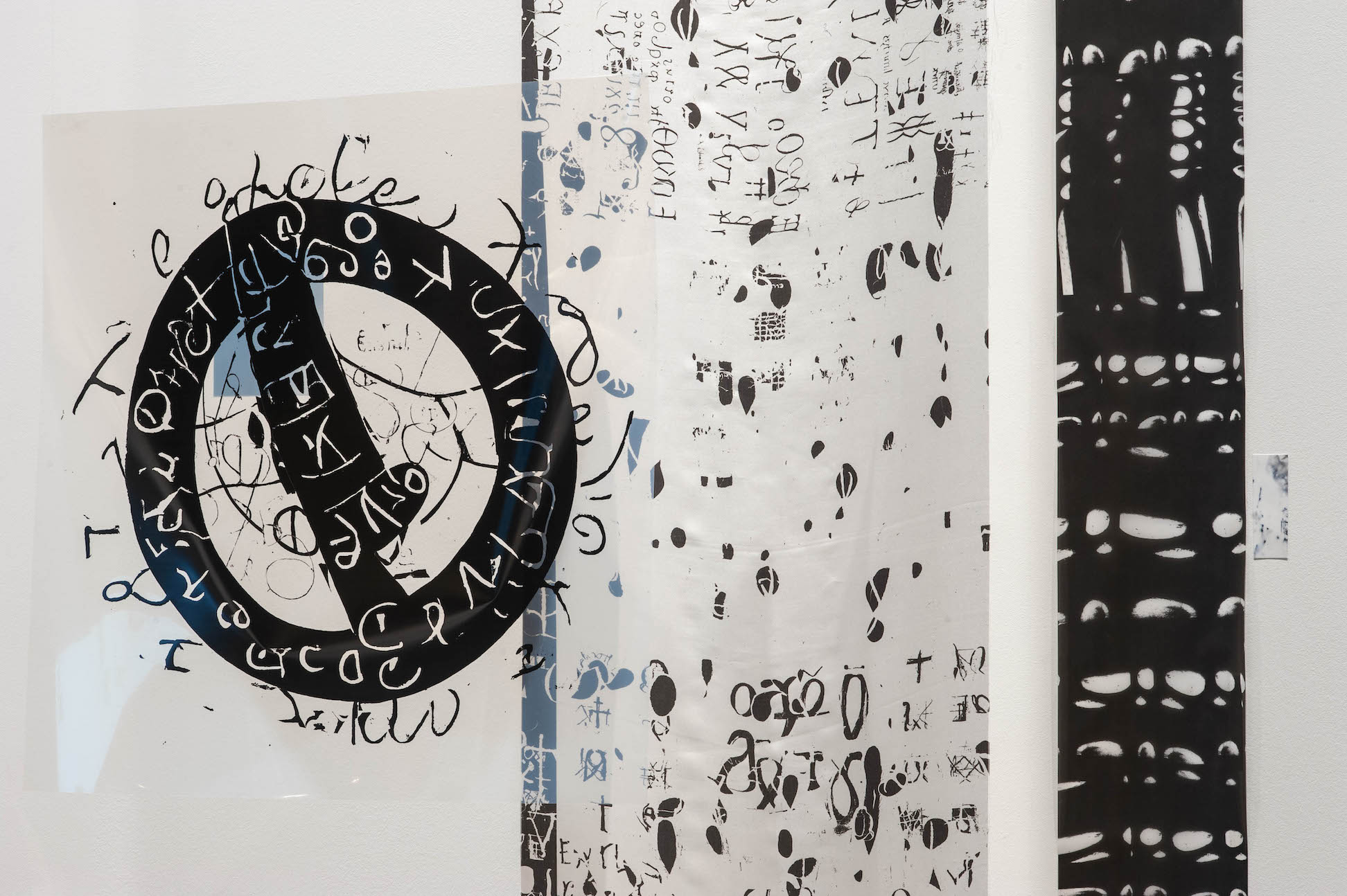 There are two vertical black and white artworks with small different black shapes and letters in different languages. On the left, there is a bold black circle with similar symbols in white.