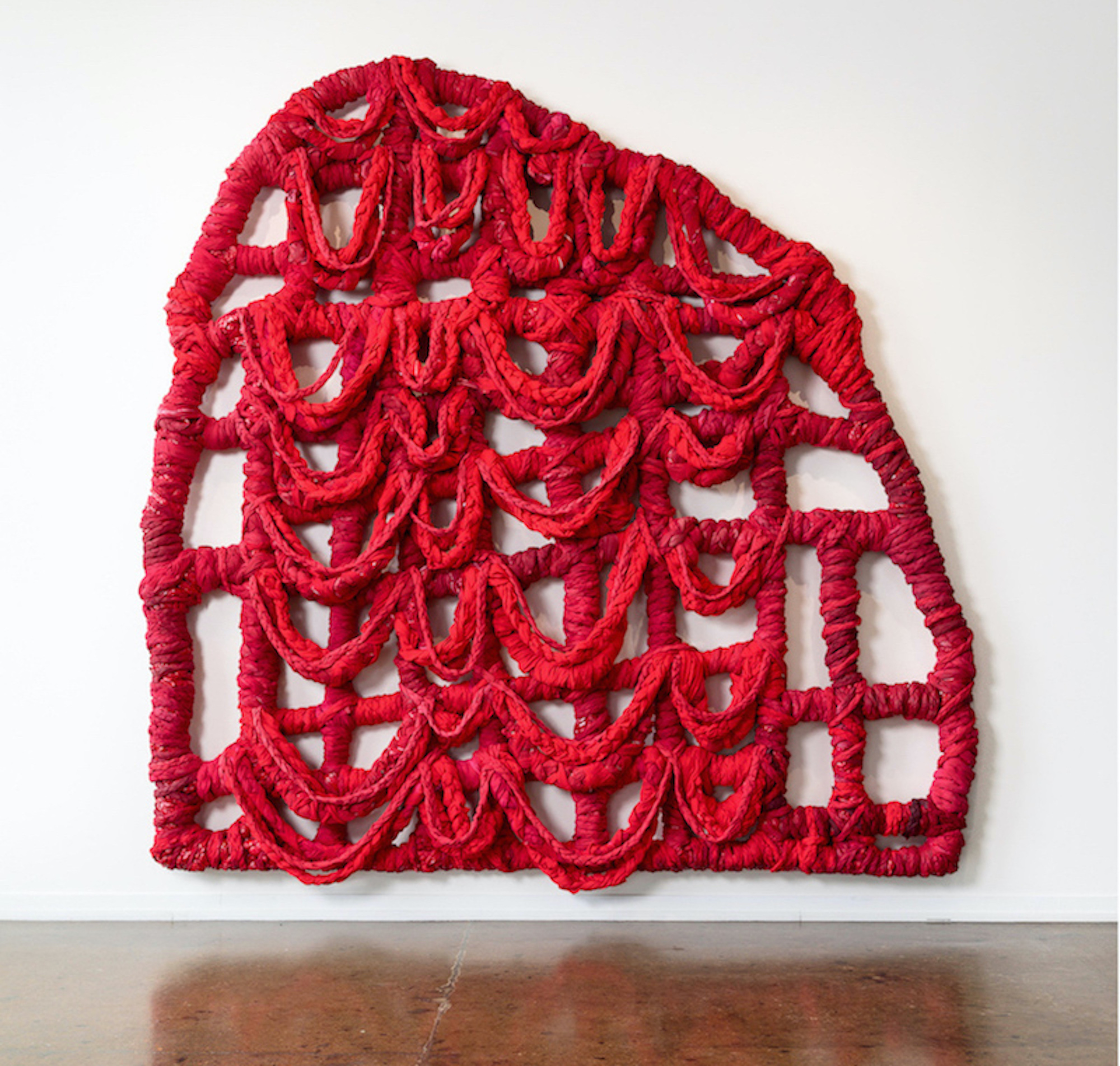 A large amorphous gate of braided sheets dyed red and draped together in the form of a grid.
