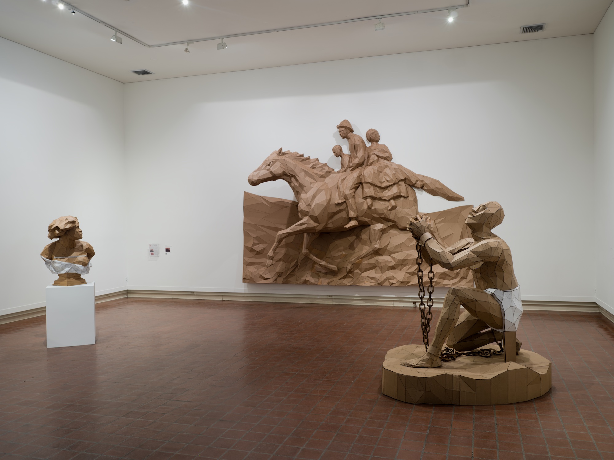 Three sculptures of cardboard depicting a a chained slave pleading upwards, the bust of a woman, and people riding upon a horse.