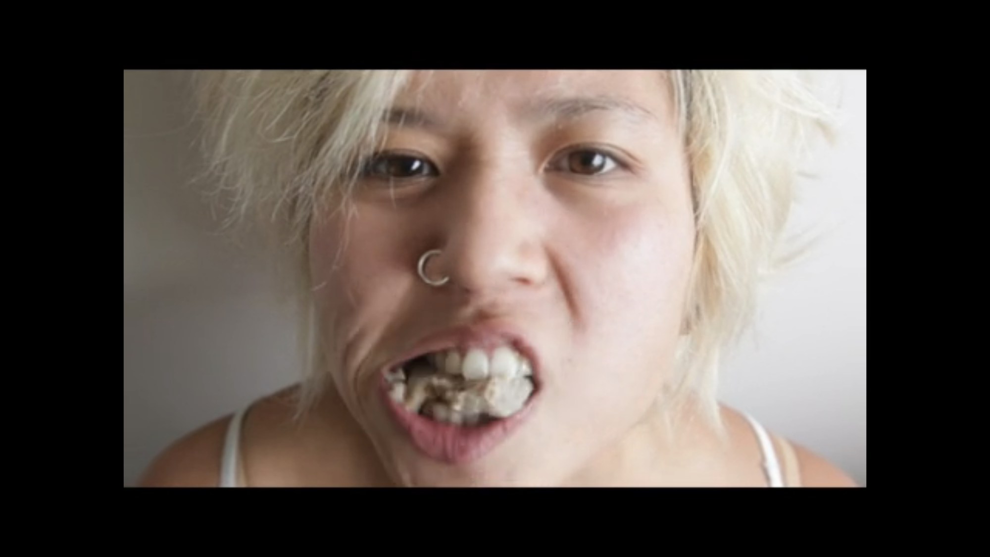 A young person with their mouthful of grayish meatballs is caught mid-chew, looking intently into the camera with a certain defiance.