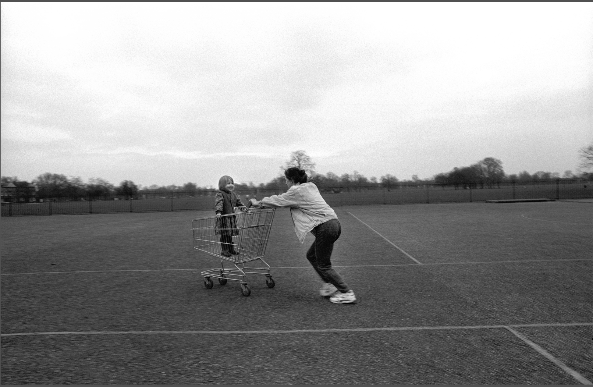 A black and white image with a woman in the center of the composition pushing a child in a shopping cart