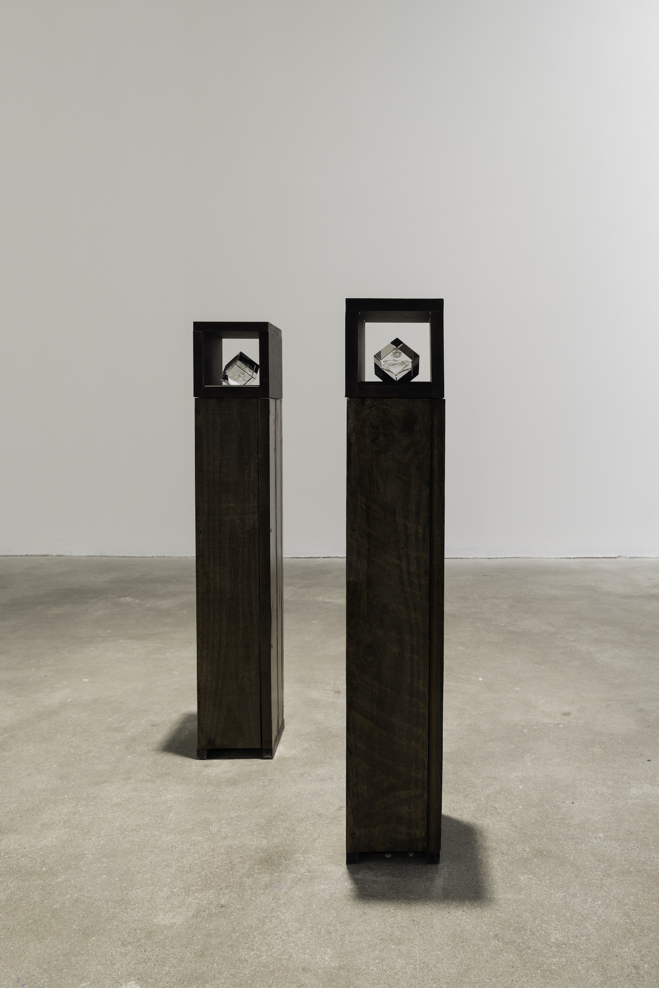 wo slim brown pedestal sculptures with side openings across each top, with small laser - cut glass sculptures nested inside