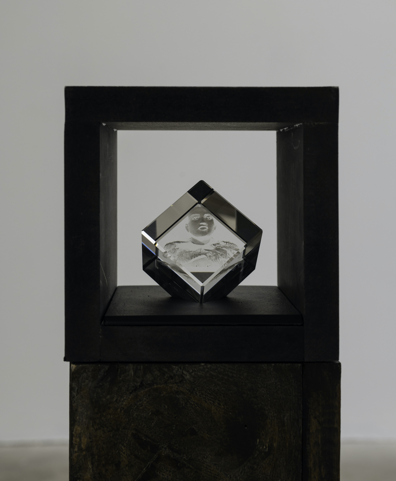 Small laser - cut glass cube sculptures nested inside the top section of brown pedestals depicting a portrait of a person