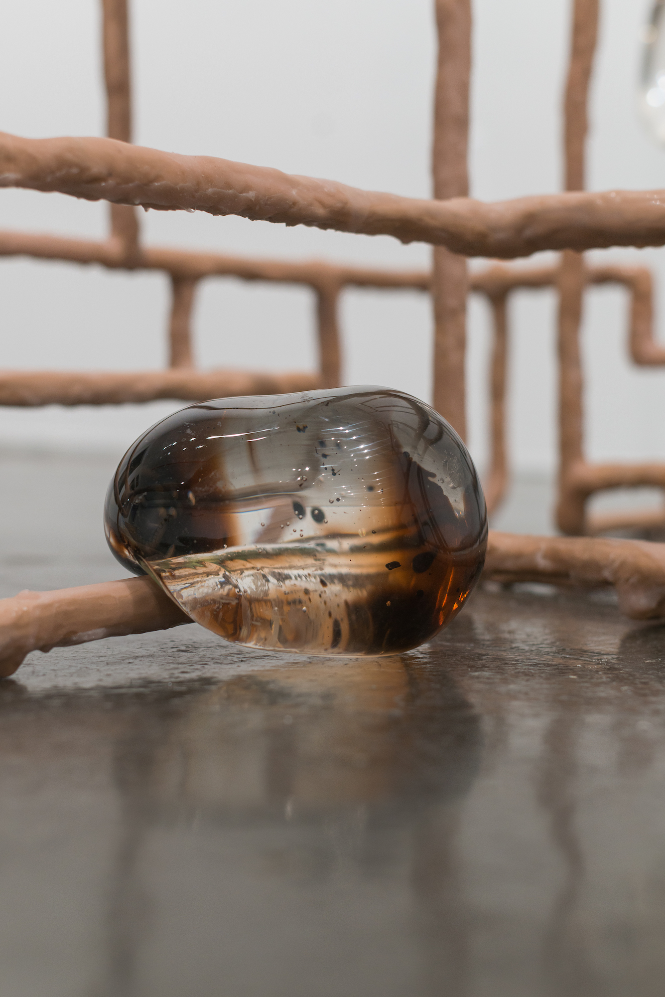 A globular piece of glass drapes over a flesh colored tube with more creating a web in the background, a dark liquid in encased in the glass.