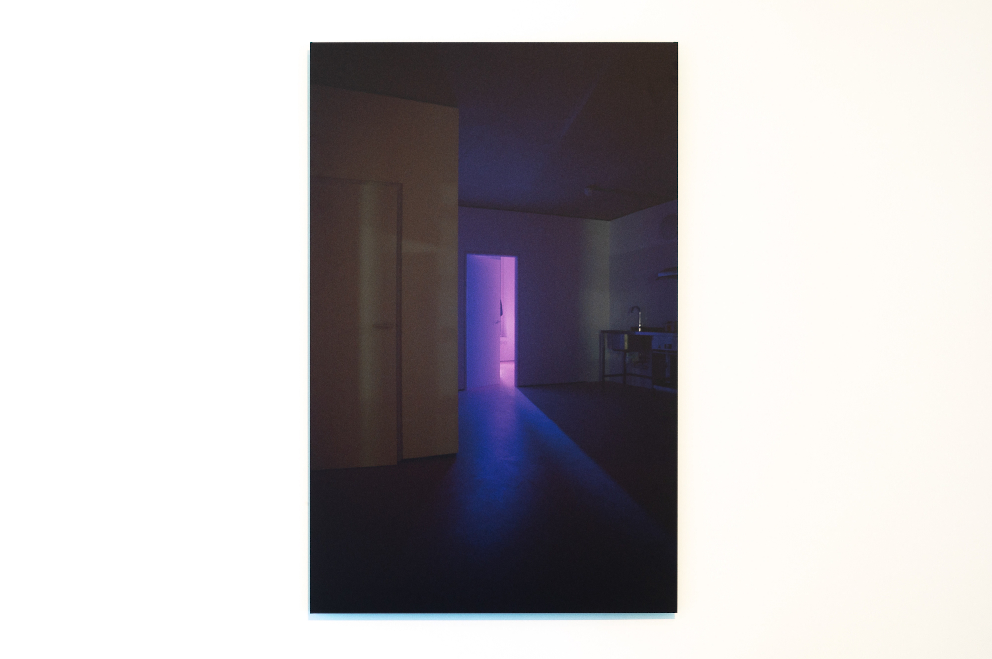A vertical rectangular photo of a silhouette of a person in a doorway in the background with a purple light emanating.
