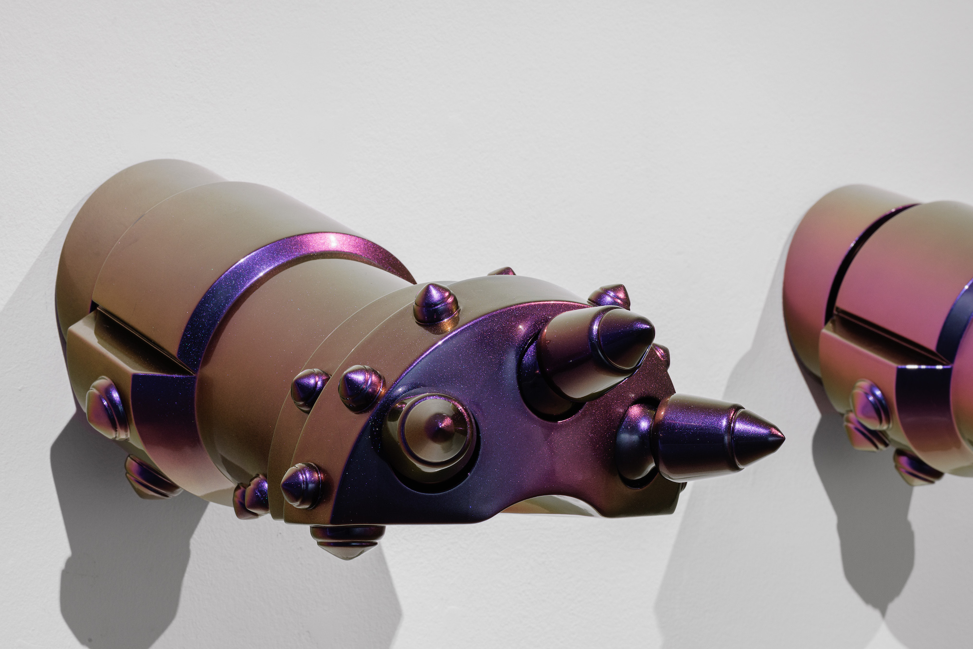 A close-up of an opalescent sculpture, shiny purple gauntlets formed from a composite of geometric structures and drill bits used for extracting petroleum.
