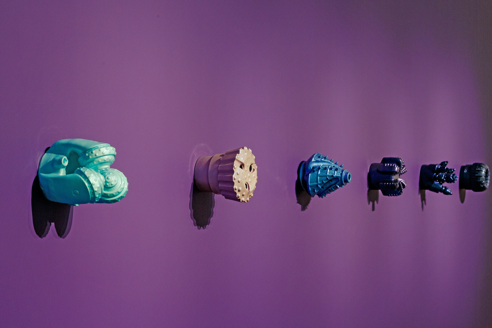 A bright purple wall with various geometric structures hung on the walls protruding out, all of them a beautiful luster of shimmering automotive paint.