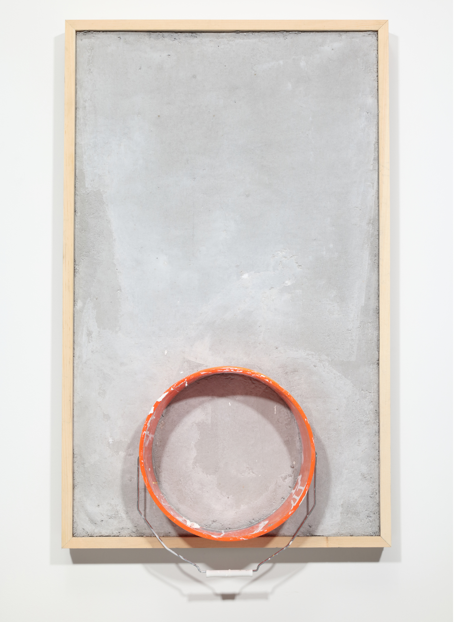 A rectangular gray concrete slab hung vertically with an orange circle of a bucket centered and embedded at the bottom.