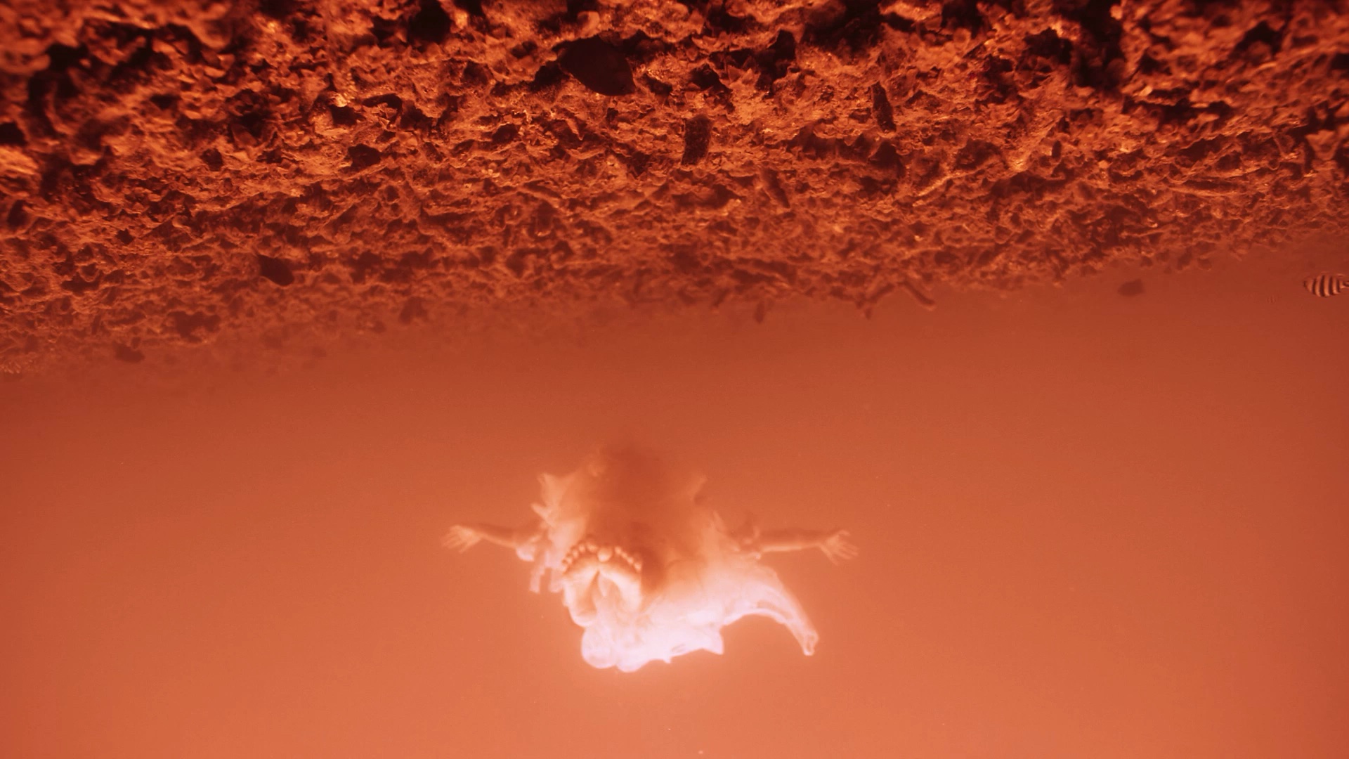 Person wearing a white outfit floating through orange liquid