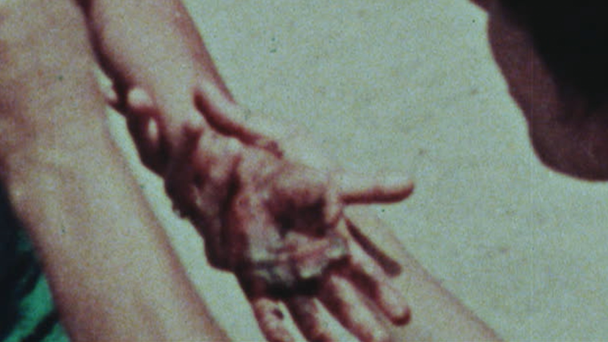 A grainy image of someone holding another person's wrist, their hands stained with a dark liquid