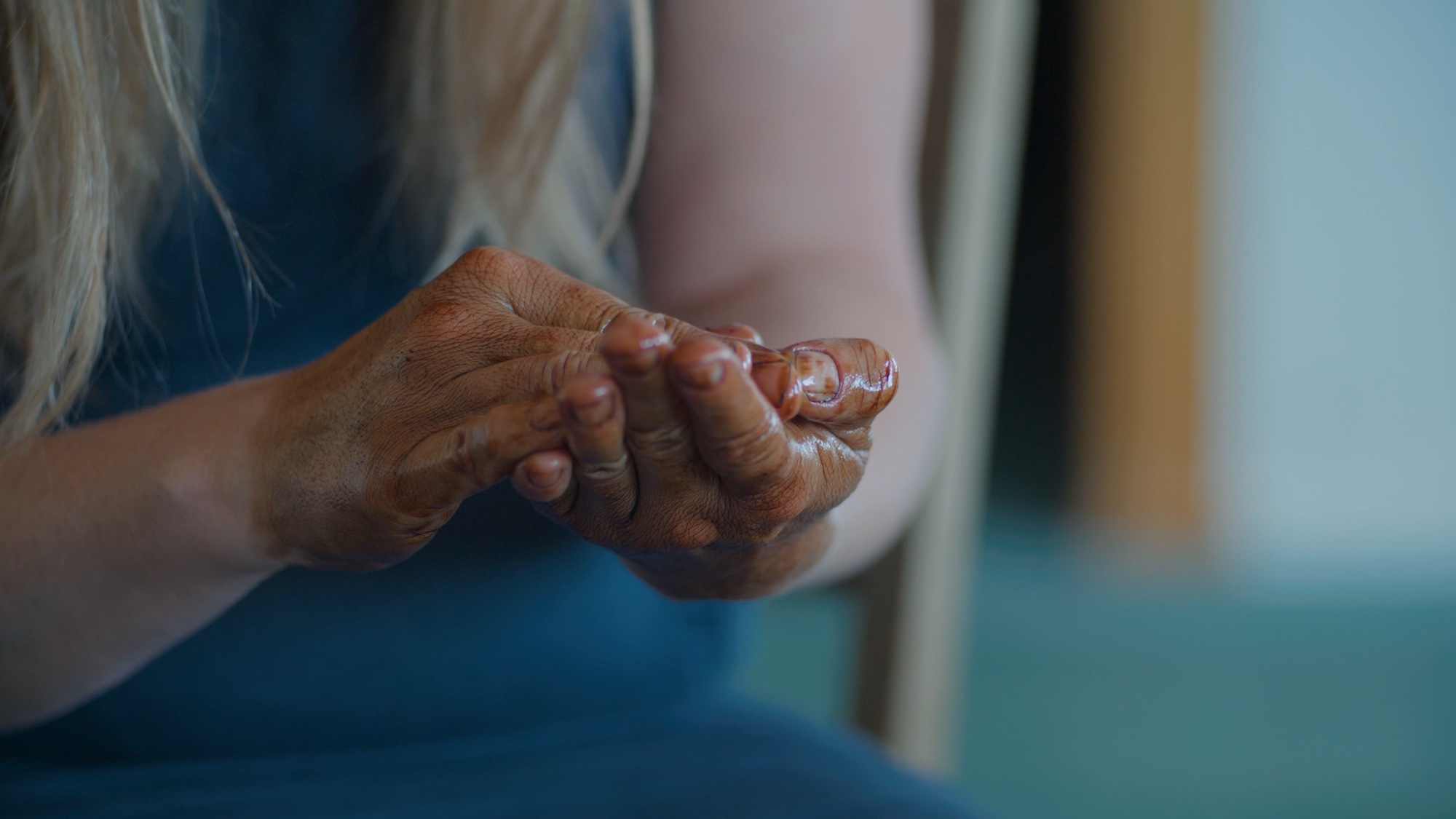 A person is rubbing their hands together, both stained in a dark liquid