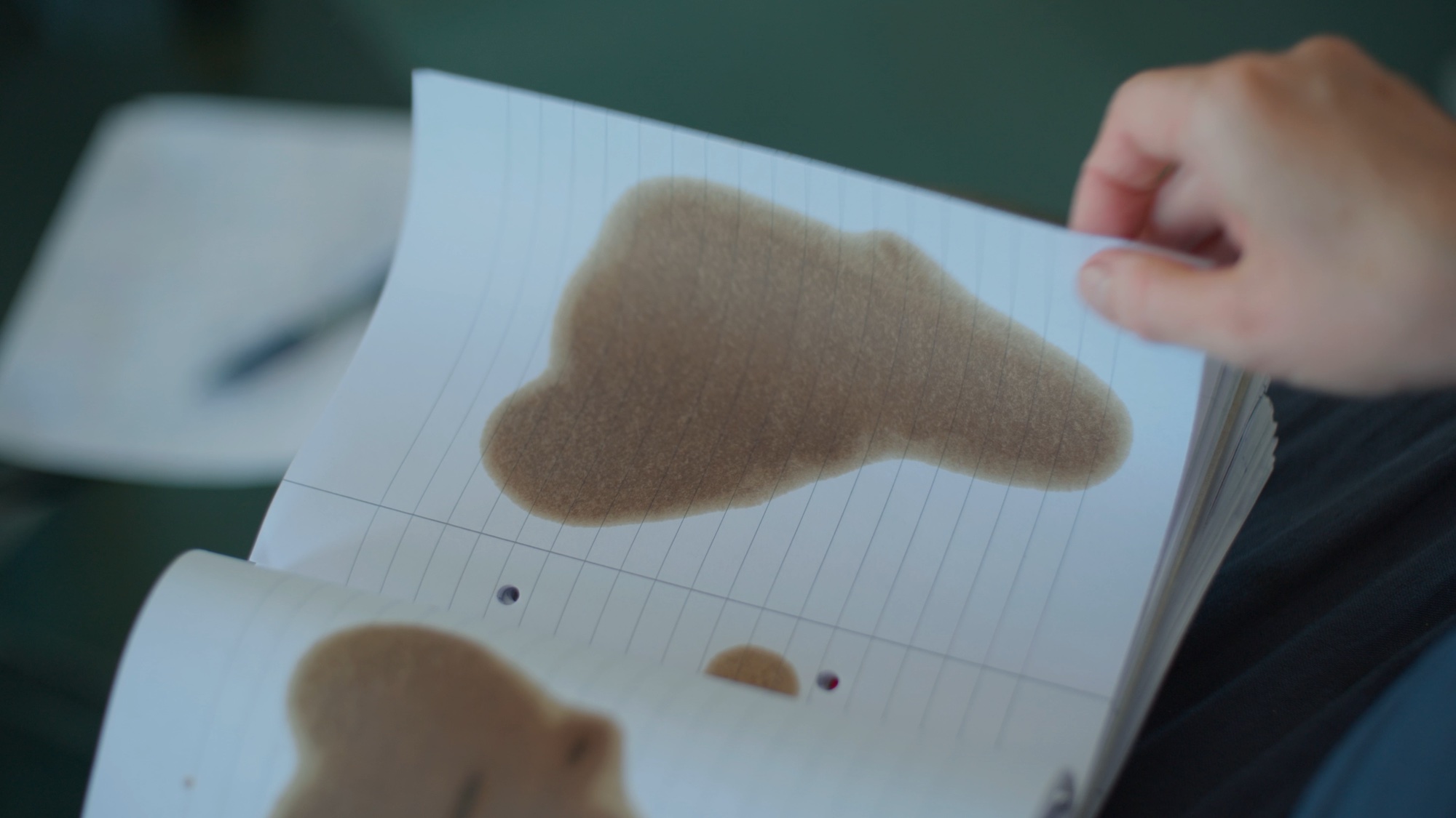 A hand turning a page of a notebook, which has a brown stain