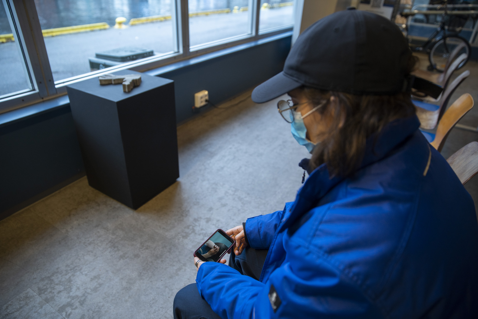 A person in a blue jacket holds a phone which depicts two hands stained in a dark liquid