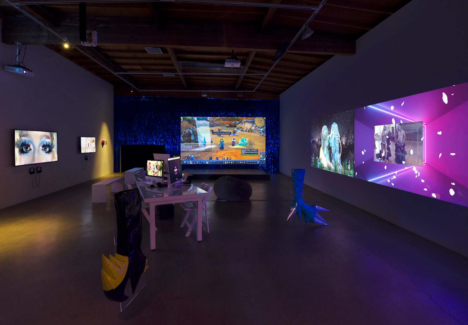 A dark room with several monitors and screens projected onto the walls, at the center of the room there is a white desk with several desktop computers open and lit up.