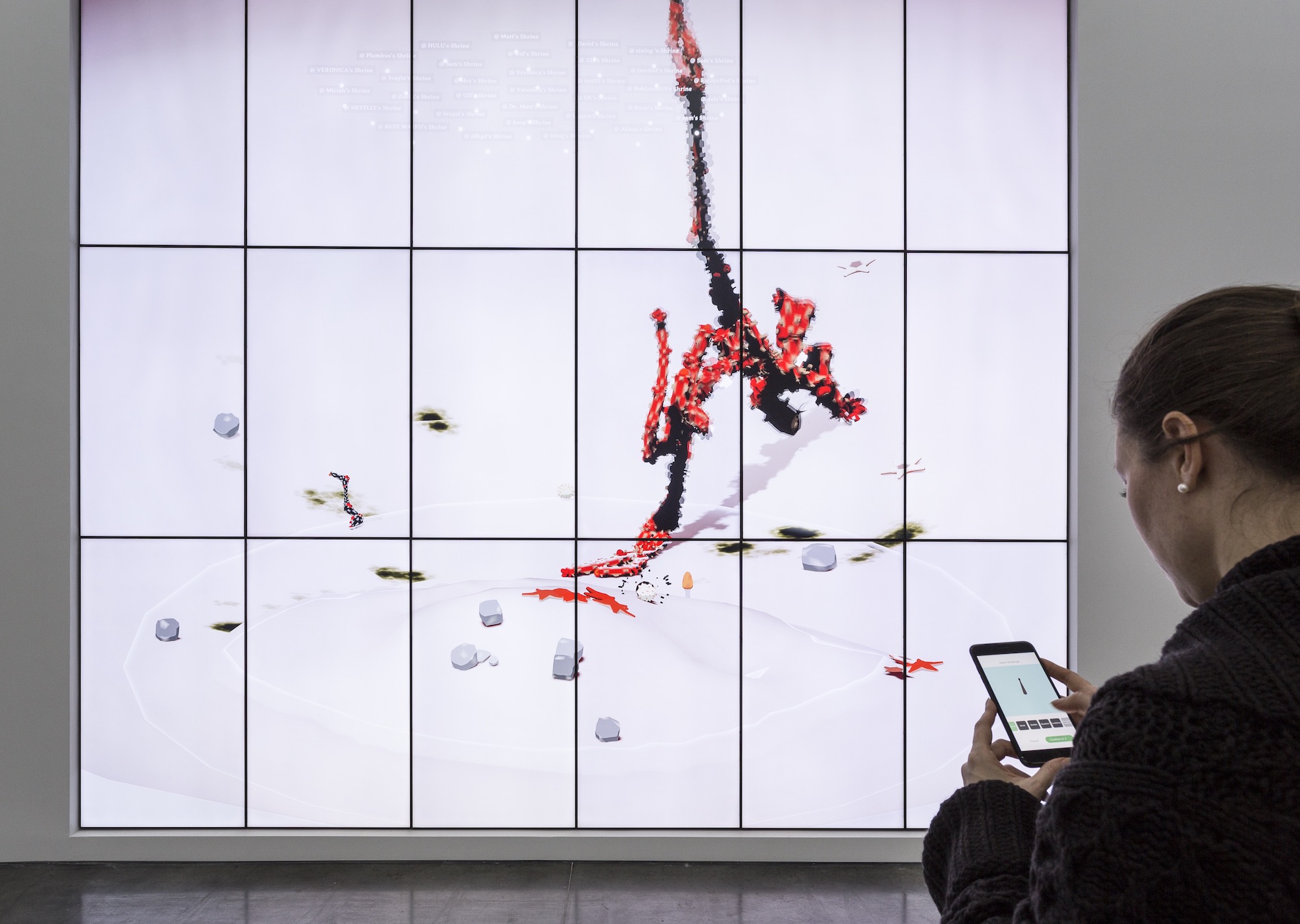 Image of a screen with a grid, a red expanding figure, and various debris. A woman in the lower right corner is looking at her phone.