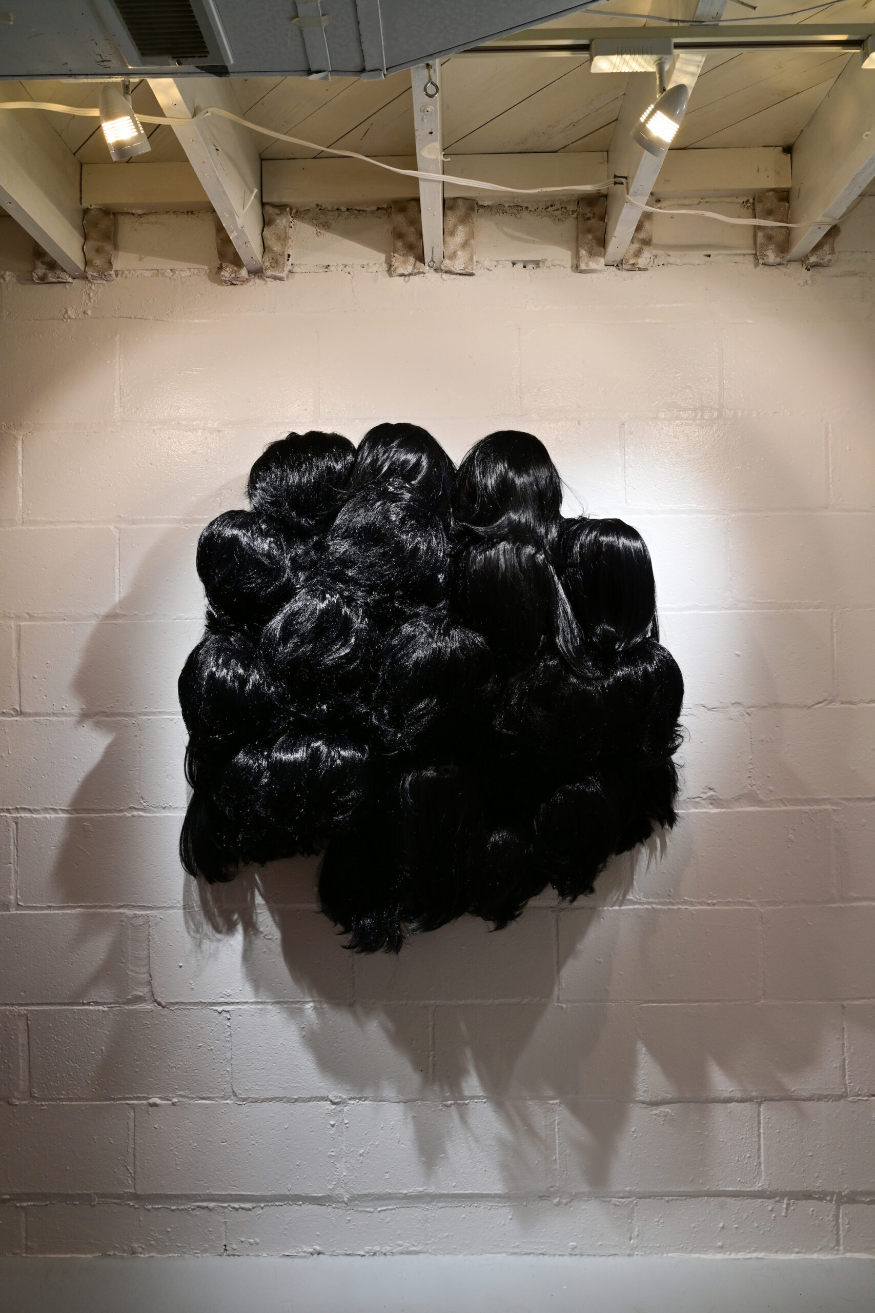 Image of a mass of dark black wigs arranged together in a vaguely spherical mass on a white stone background.
